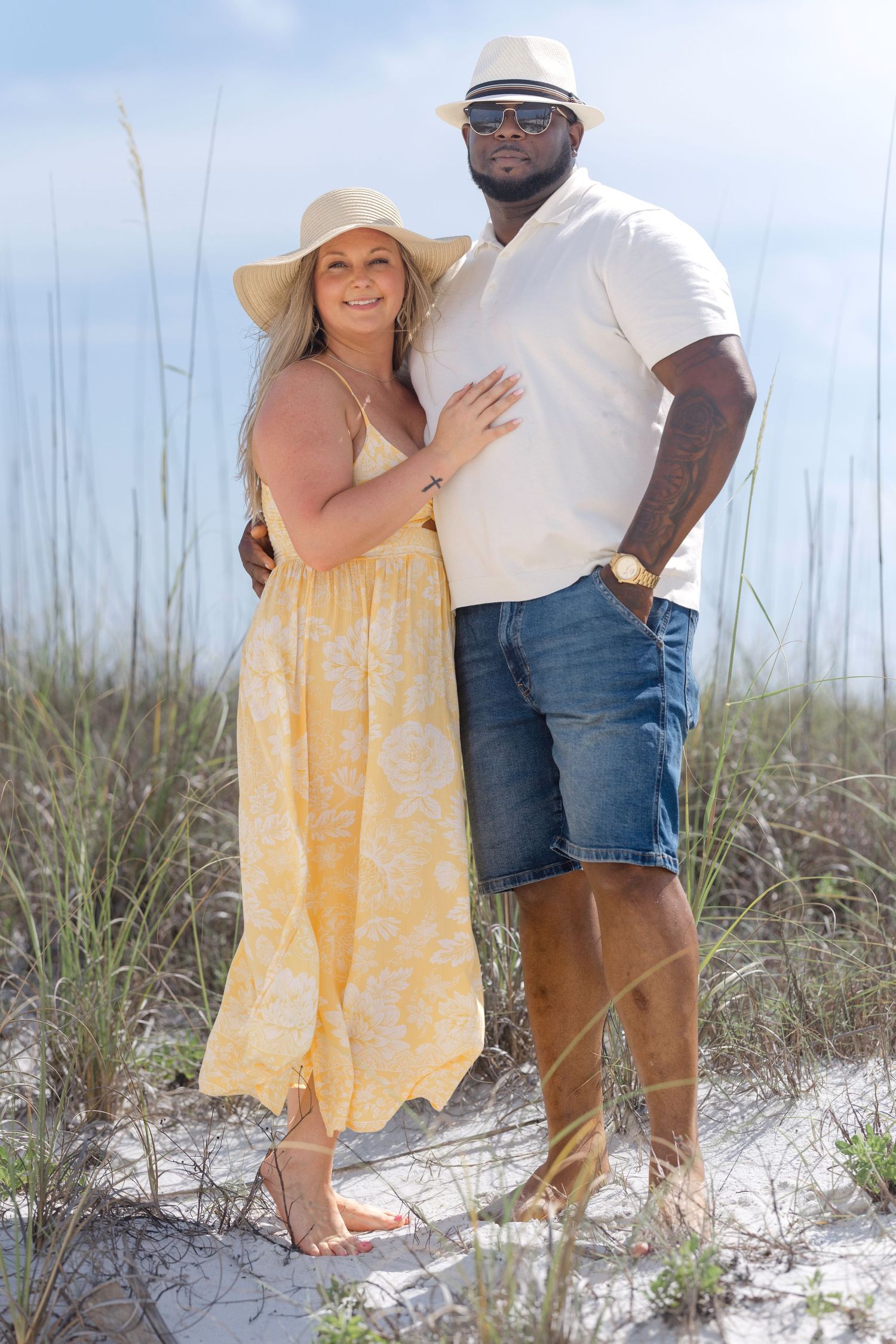 Interracial couple in matching yellow and white outfits pose together on a sandy beach dune.