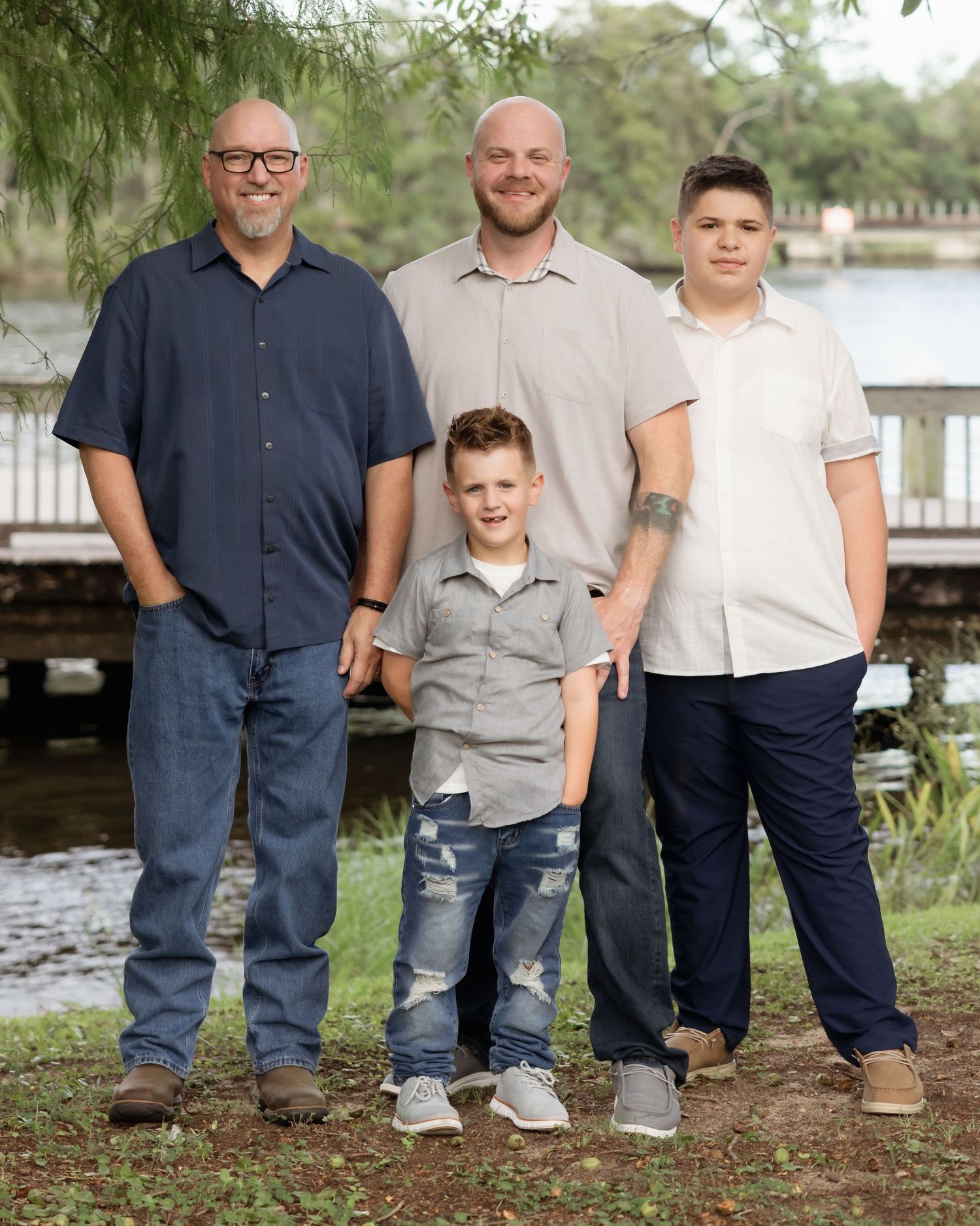 Four males posing outdoors near a lake, ranging from young boys to adults, dressed in casual family portrait attire.