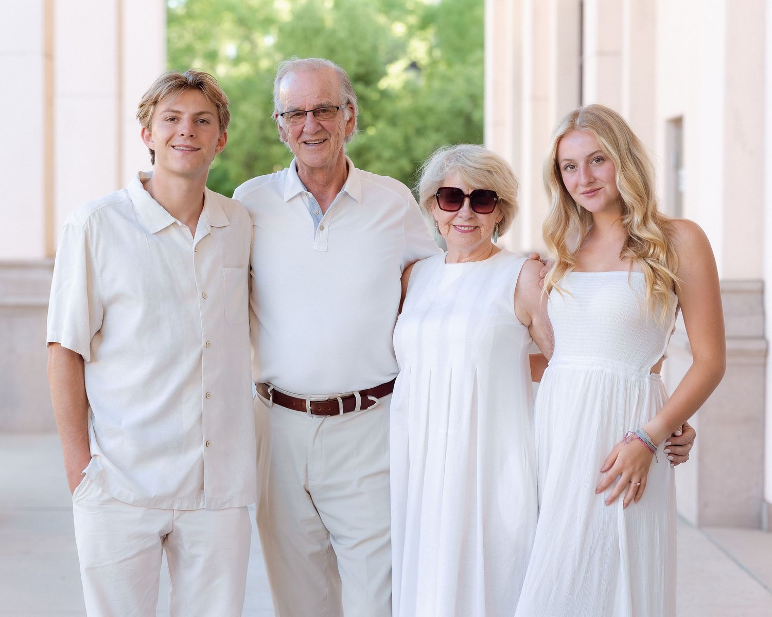 Family of four smiling together in coordinating white and cream outfits outdoors.