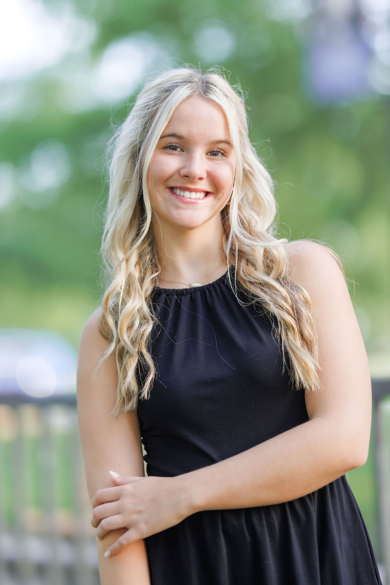 Casual outdoor photoshoot featuring a black sleeveless top against a green natural background.