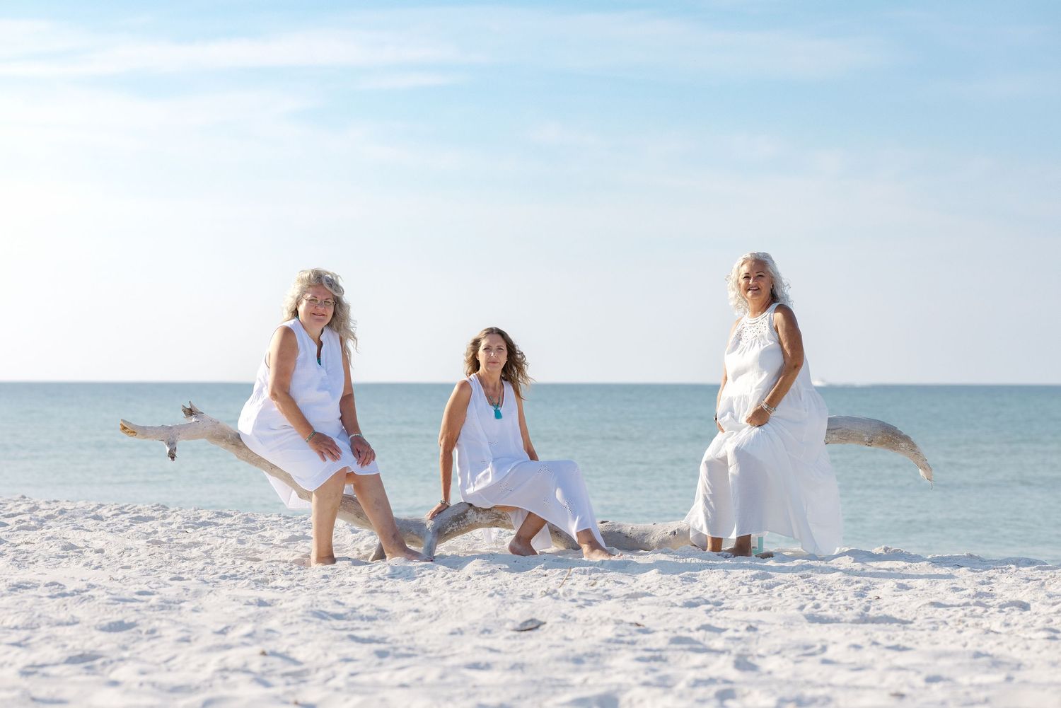 Four white-clad beachgoers enjoy a playful moment together on pristine white sand by the ocean.