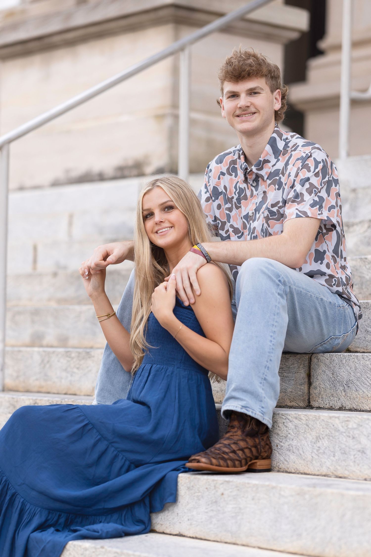 A couple in coordinated outfits lounges casually on outdoor stone steps during a photo session.
