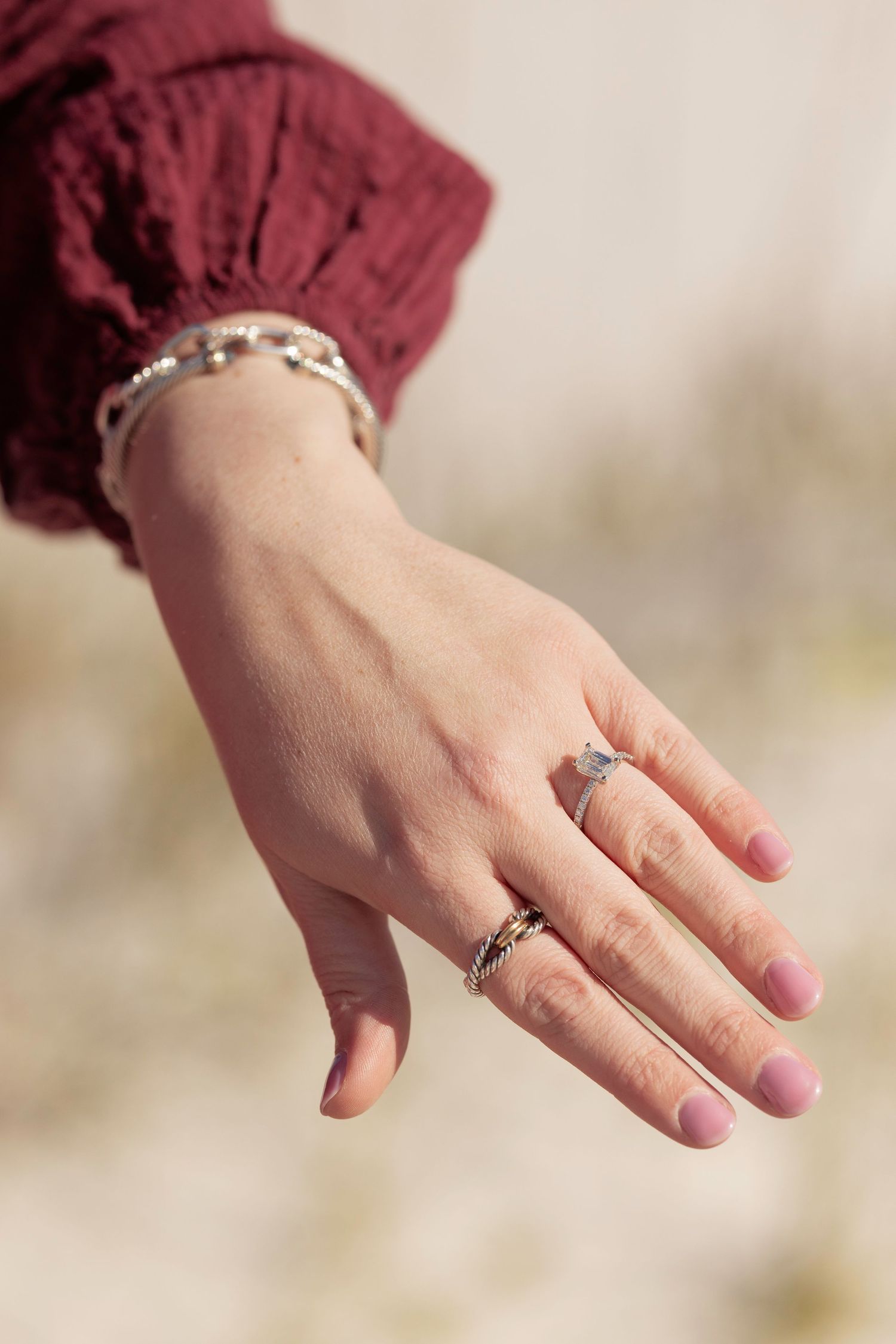 Close-up of a woman's hand displaying elegant silver rings and a beaded bracelet, wearing a burgundy sleeve.