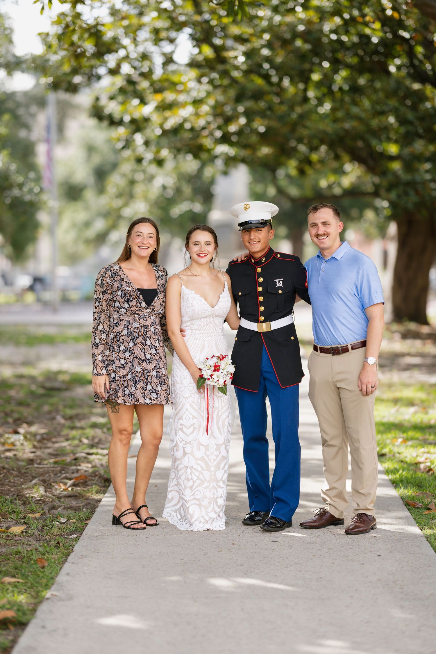Bride and Marine groom pose with family on a tree-lined sidewalk on their wedding day.