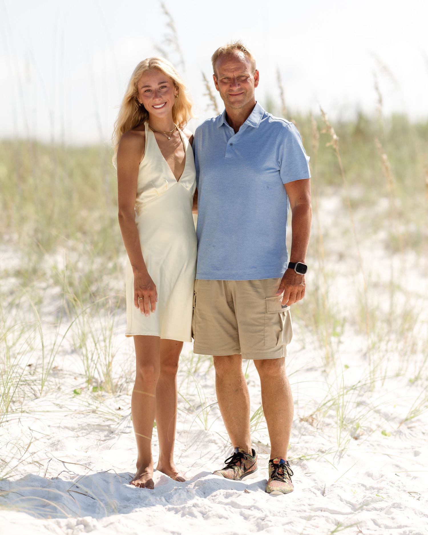 Smiling couple posing together on sandy beach dunes.
