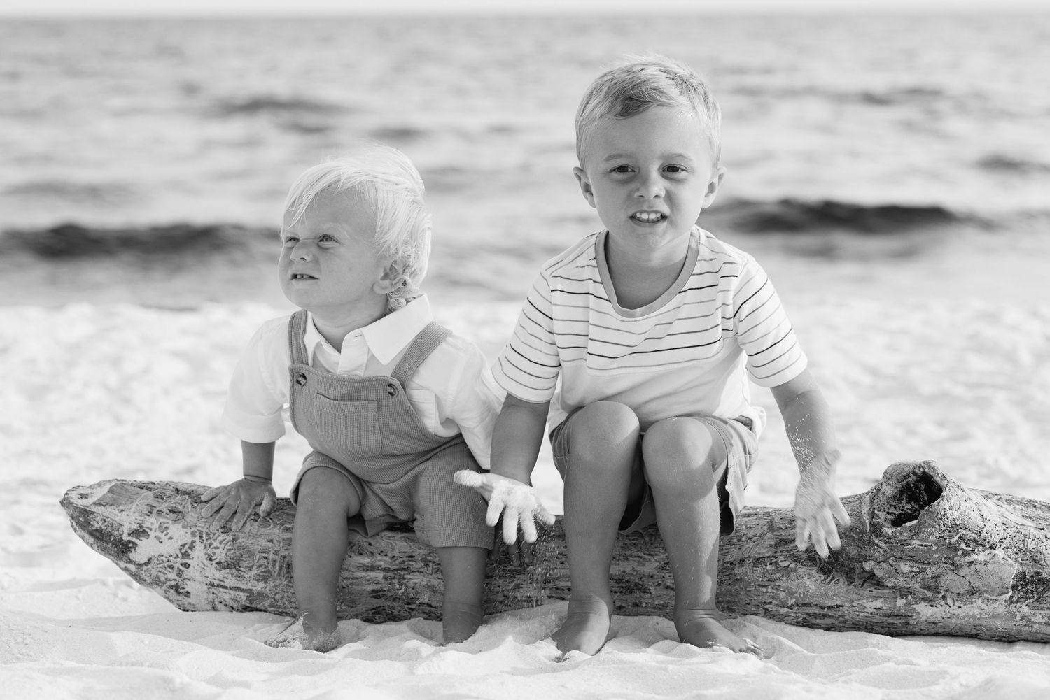 Five black and white photos show babies and toddlers playing together on a beach in the sand.