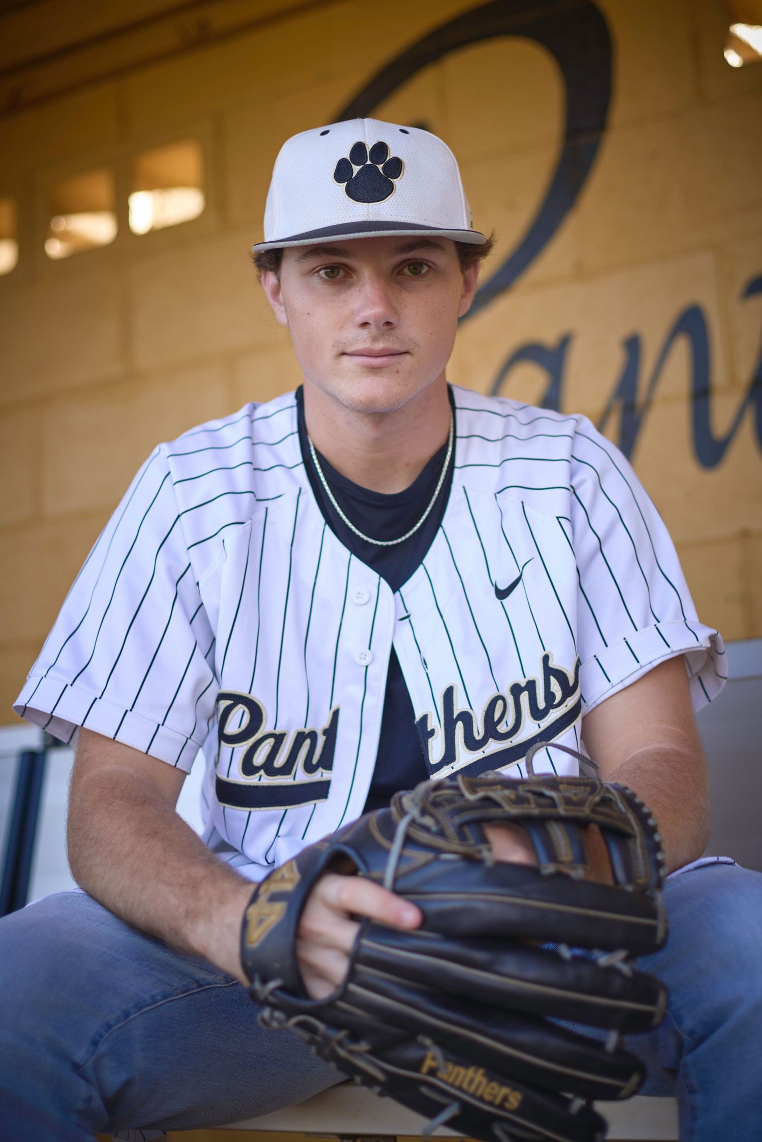 Baseball player in Panthers uniform displaying baseball glove while sitting in dugout.