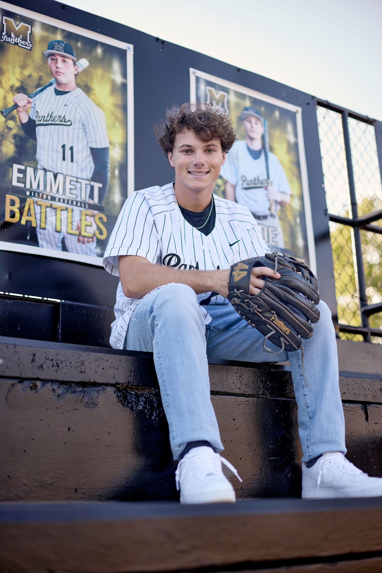 Baseball player sitting on dugout bench wearing pinstripes and holding a glove in casual pose.