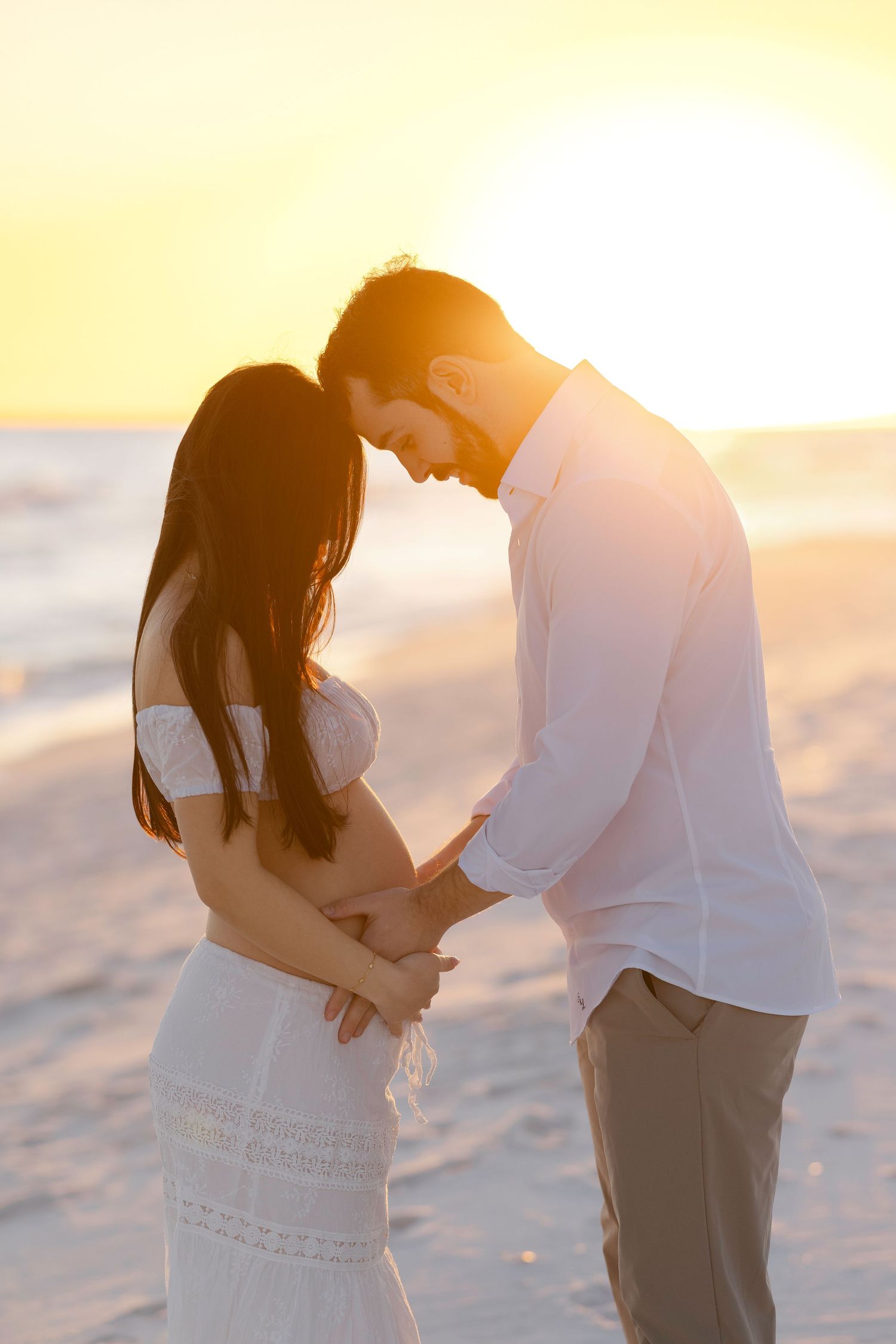 A romantic couple shares an intimate moment on the beach during golden hour sunset.