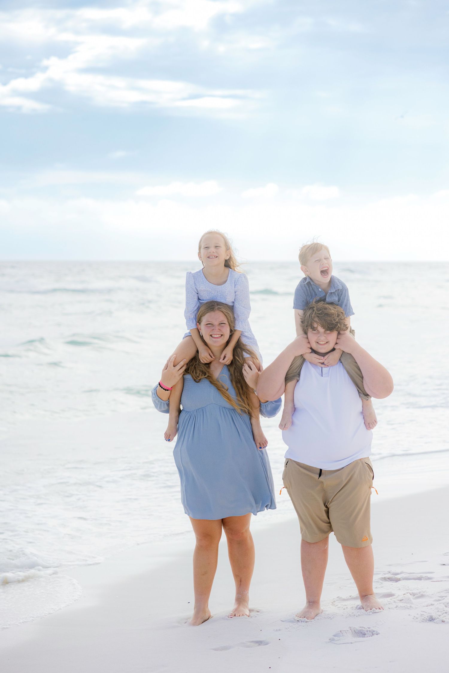 A couple wearing blue and beige outfits holds hands while walking together on a sunny beach.