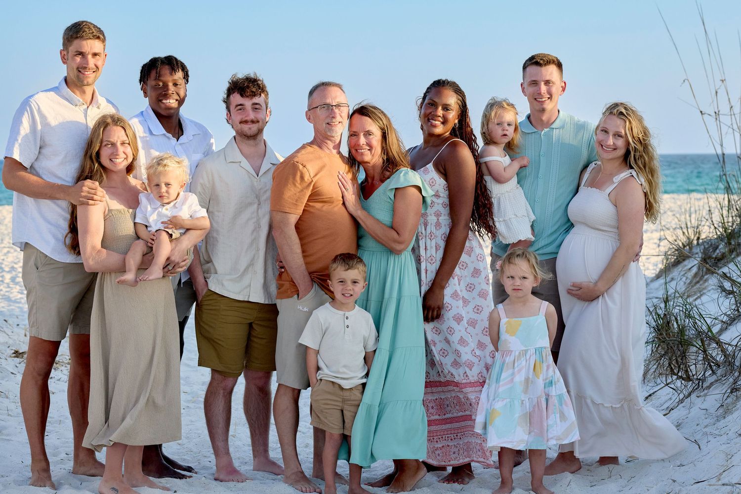 Large family group posing together on a sandy beach with turquoise ocean water in the background.