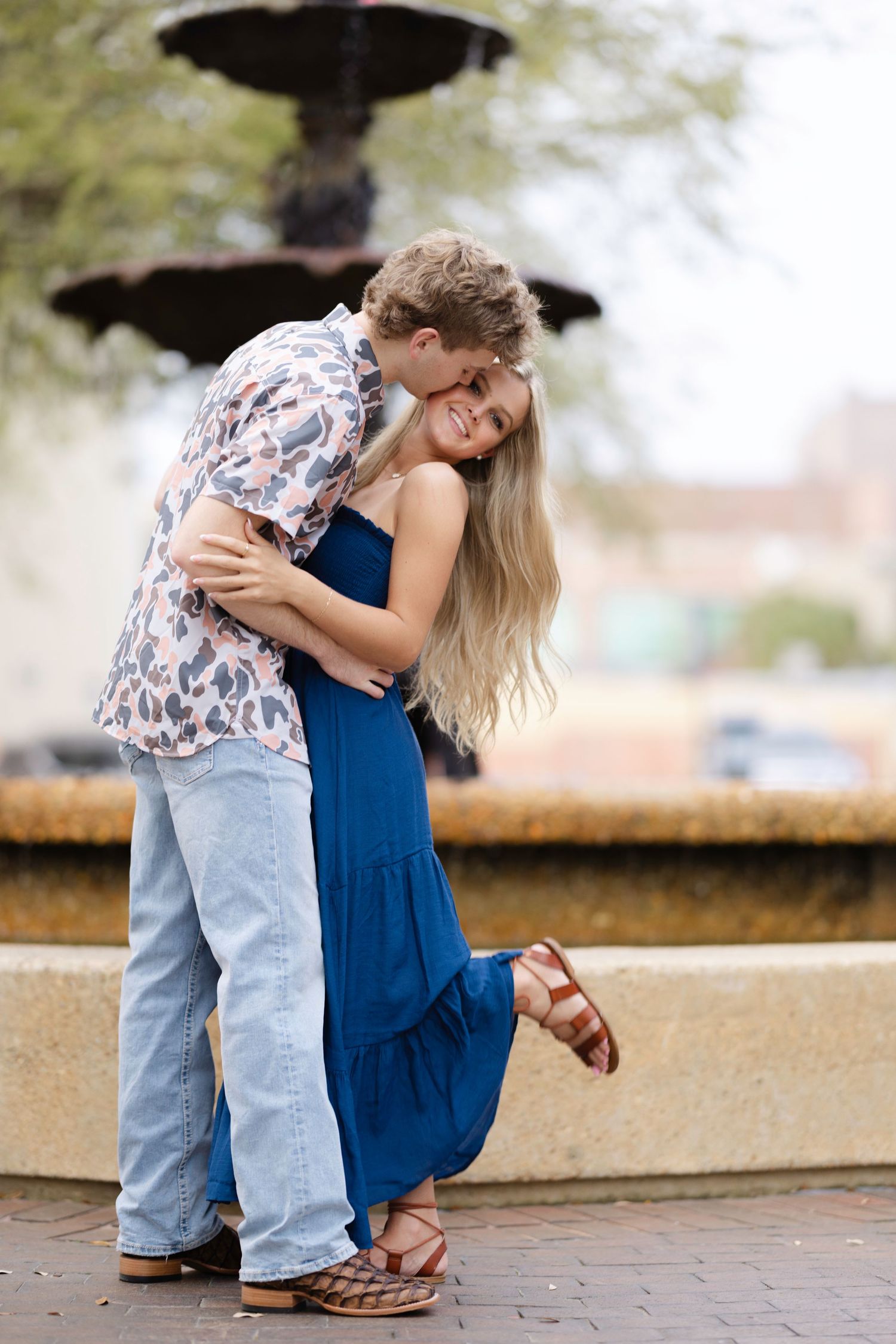 A couple in casual attire sharing a tender moment together outdoors on a brick walkway.