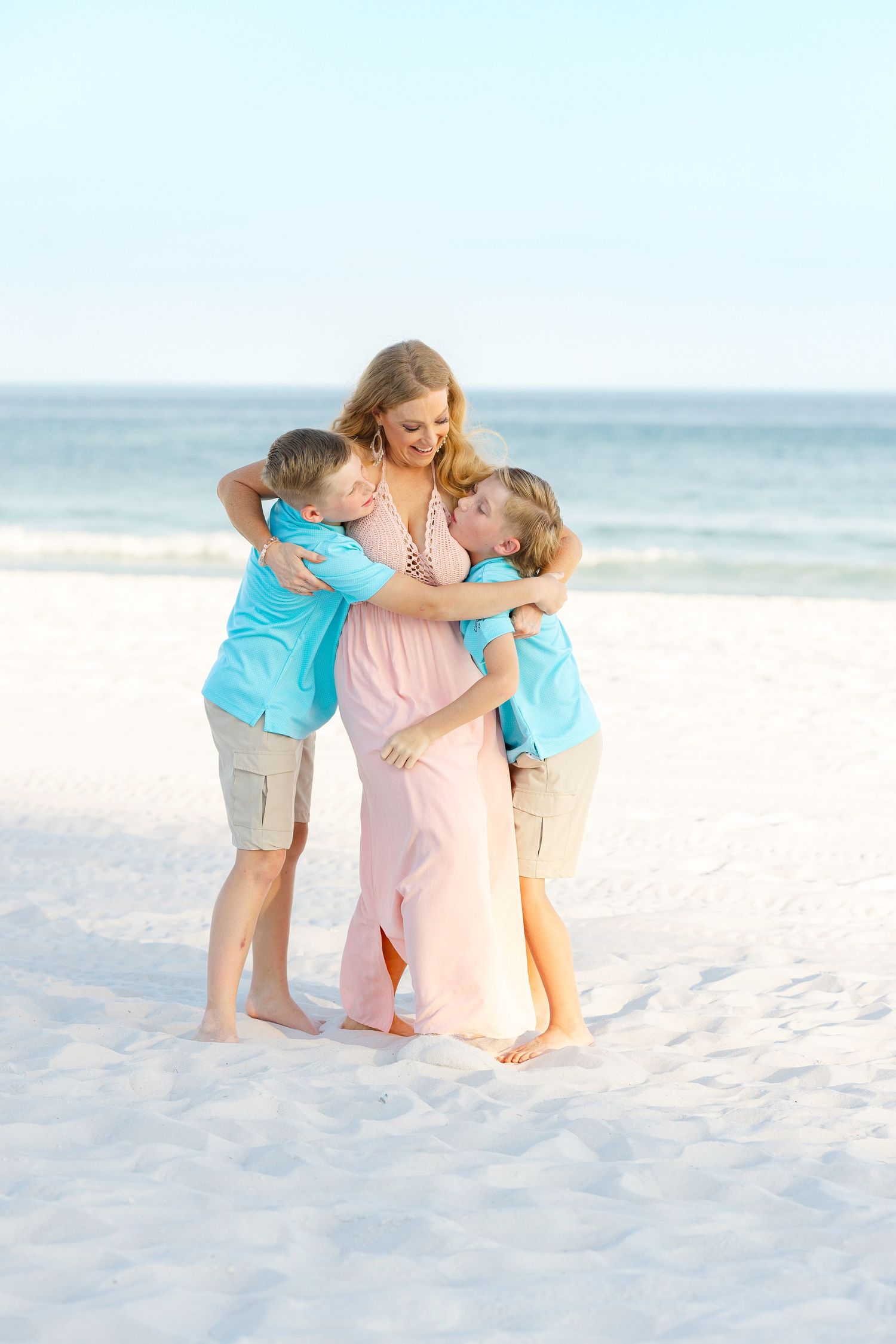 A tender moment of embrace on a white sandy beach with the ocean in the background.
