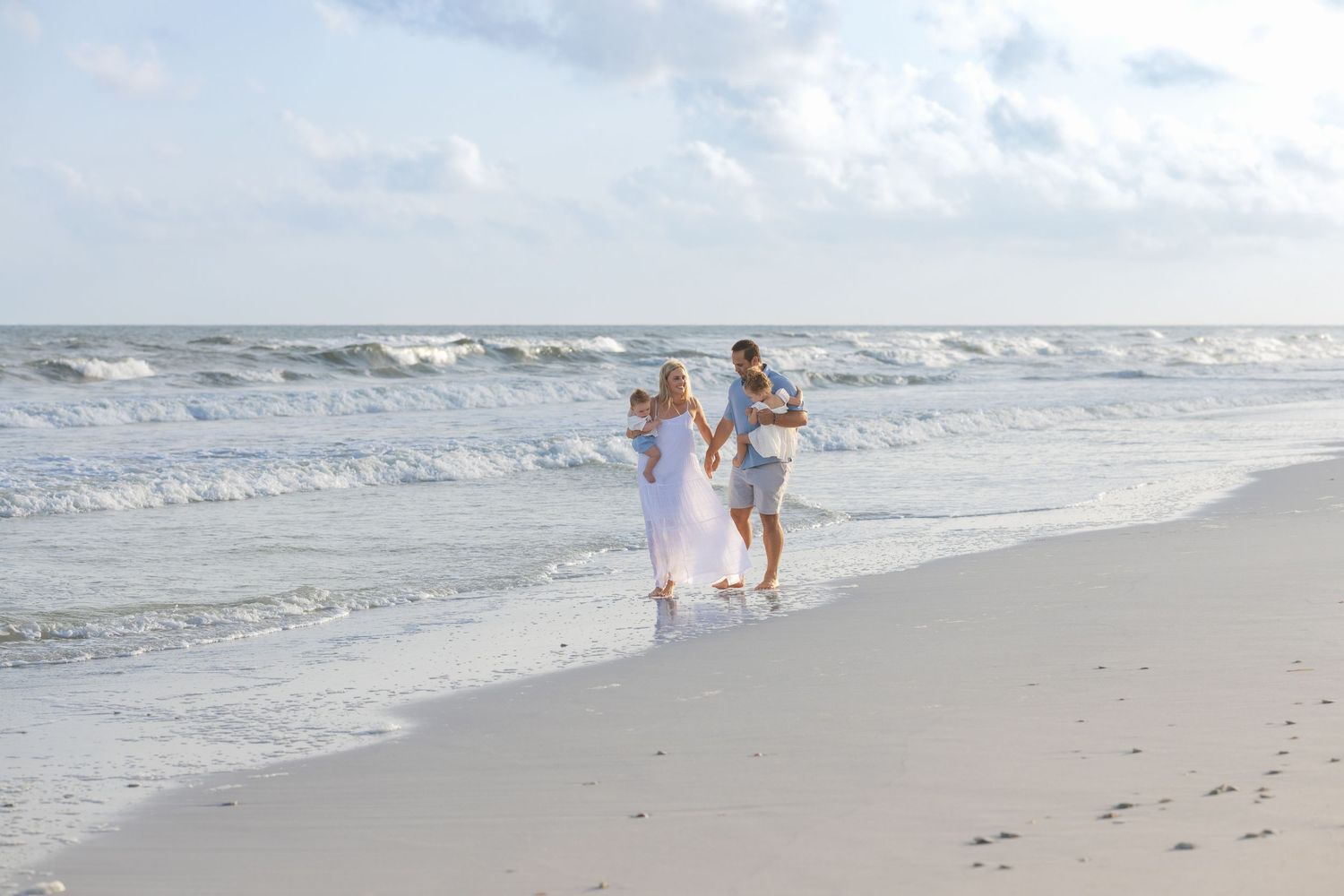 Family walking along a sandy beach near ocean waves, parents and child enjoying a sunny day by the shore.
