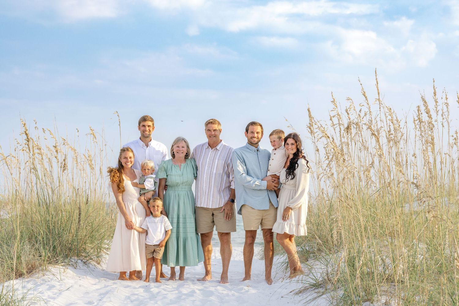 Family of eight posing together on a sandy beach with sea oats and blue sky backdrop.