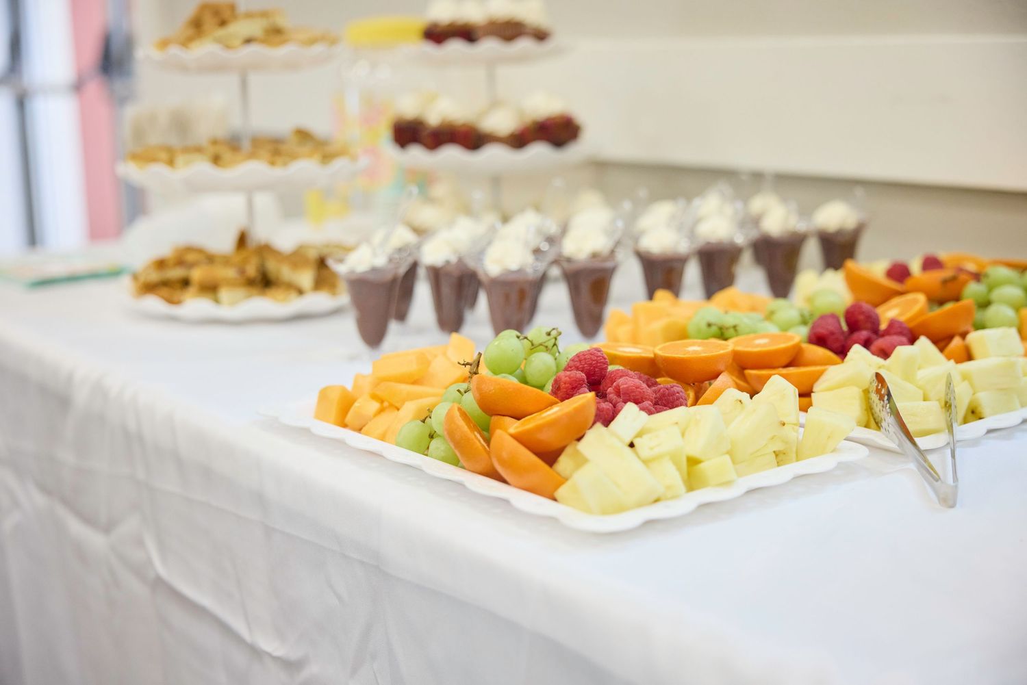 A catering display features colorful platters of fresh vegetables, fruits, and appetizers arranged on a white tablecloth.