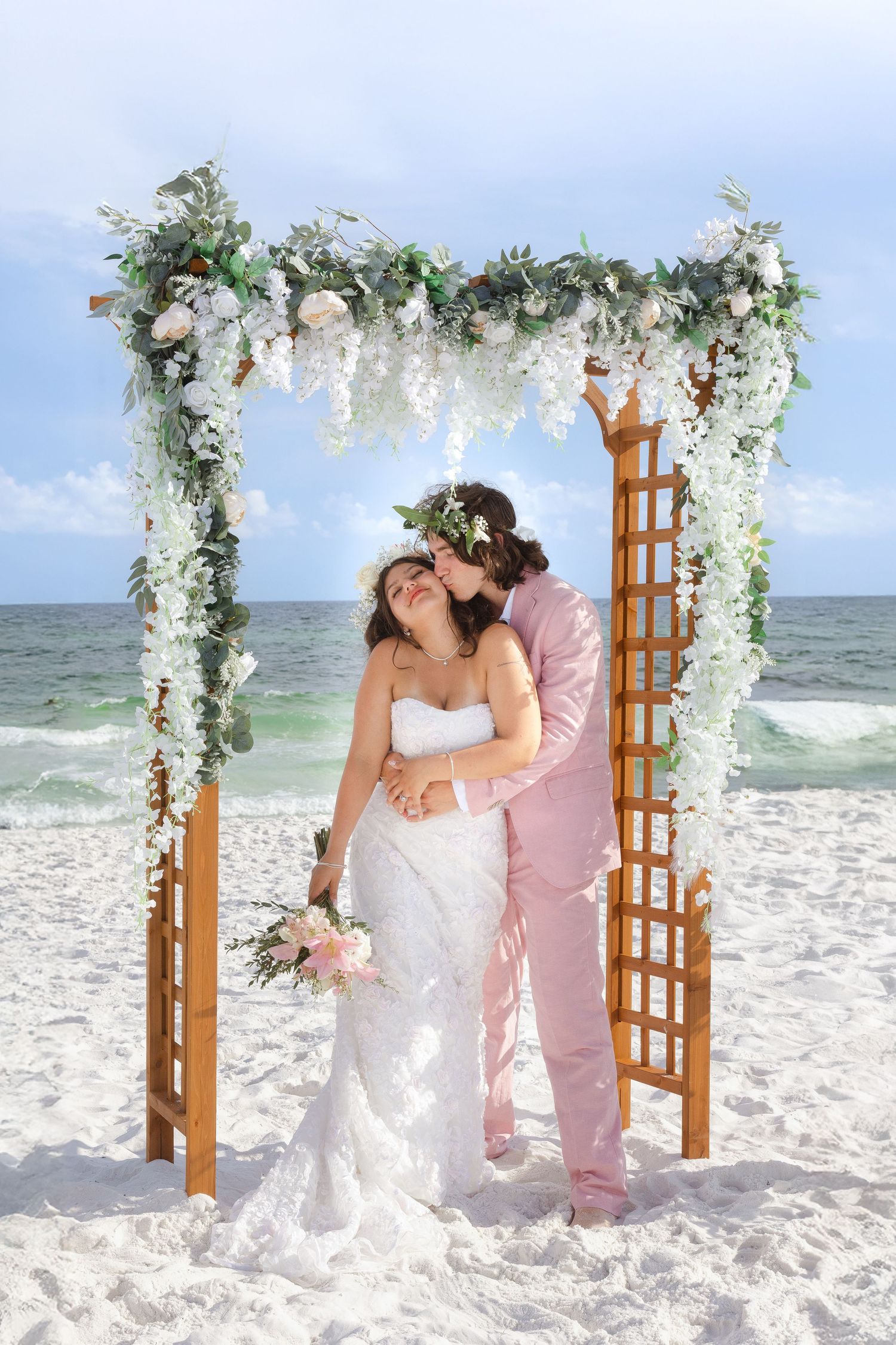 Romantic beach wedding ceremony under a floral arch with ocean waves in the background.