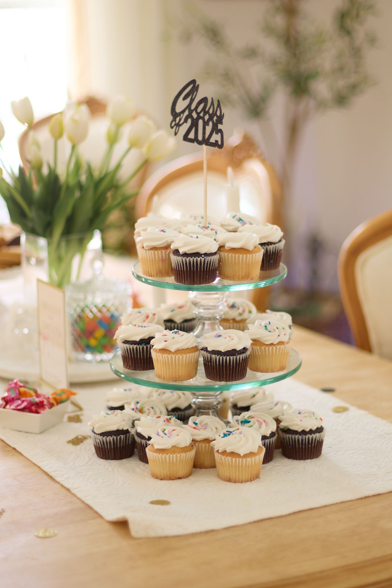 Three-tiered display of vanilla and chocolate cupcakes with a decorative topper.