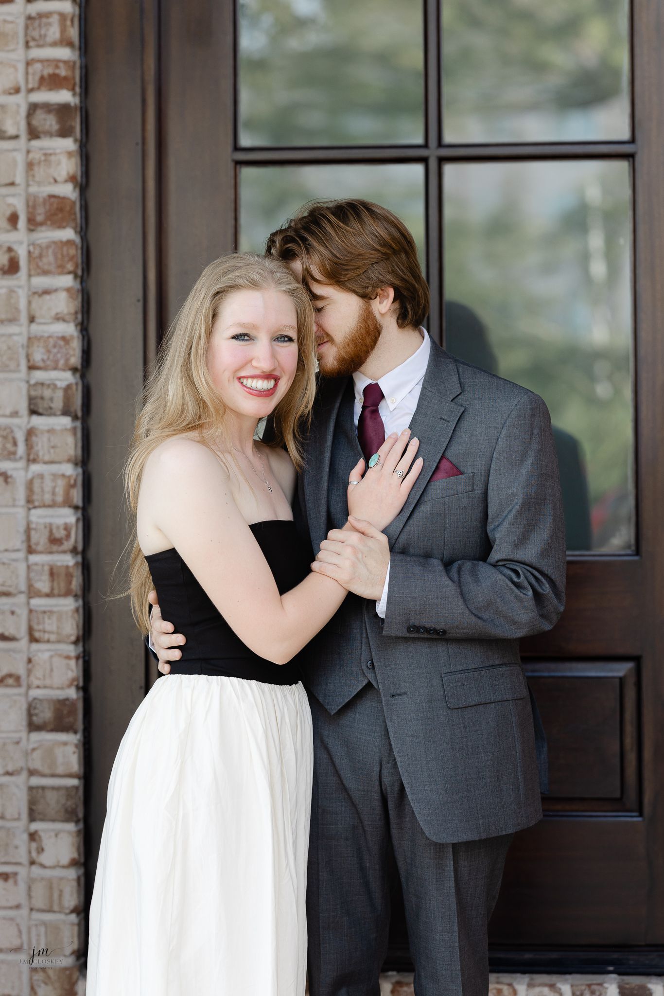 Couple in formal wear embraces in front of elegant wooden door.