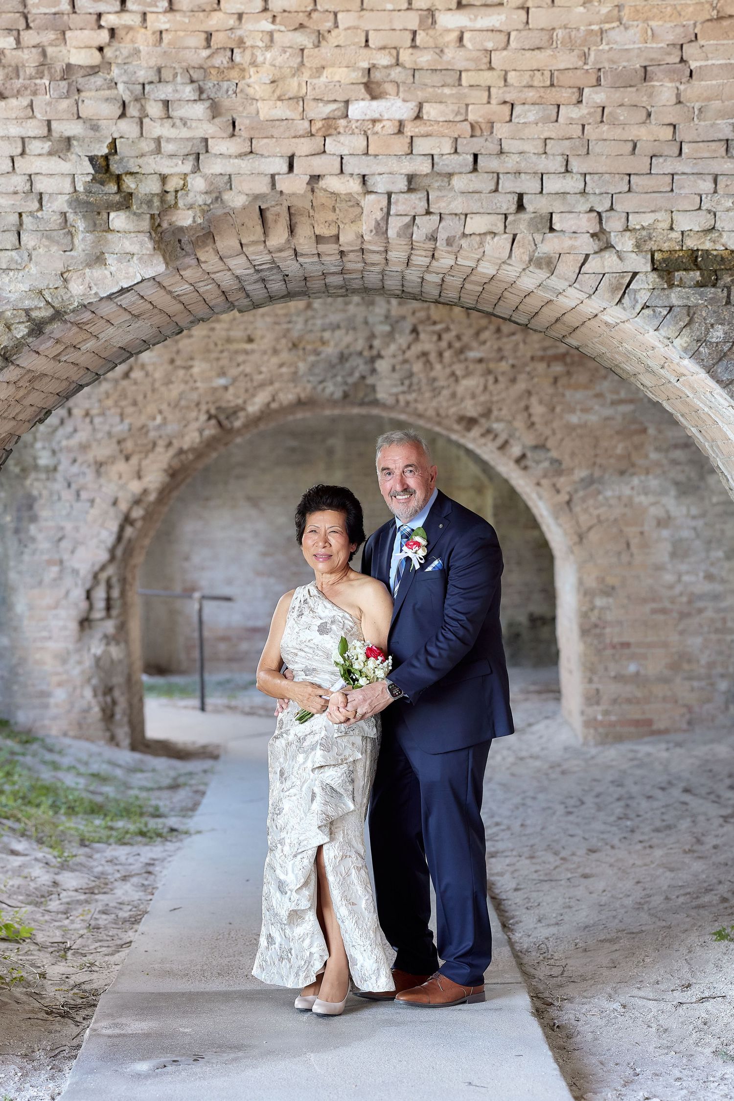 A couple poses together under a brick archway at Fort Point in San Francisco, dressed in formal wedding attire.