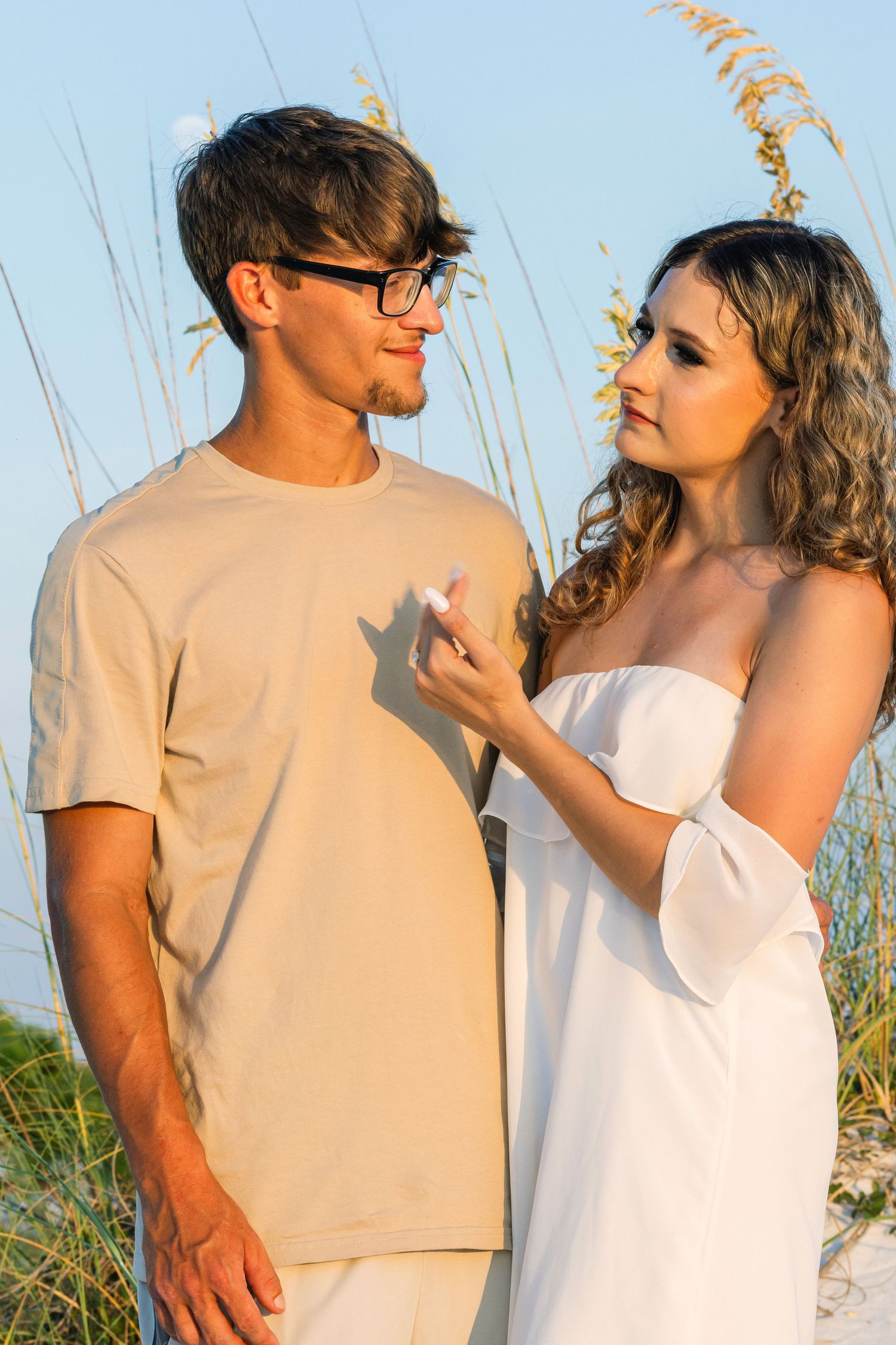 A couple in white and beige outfits shares intimate moments against beach grass.