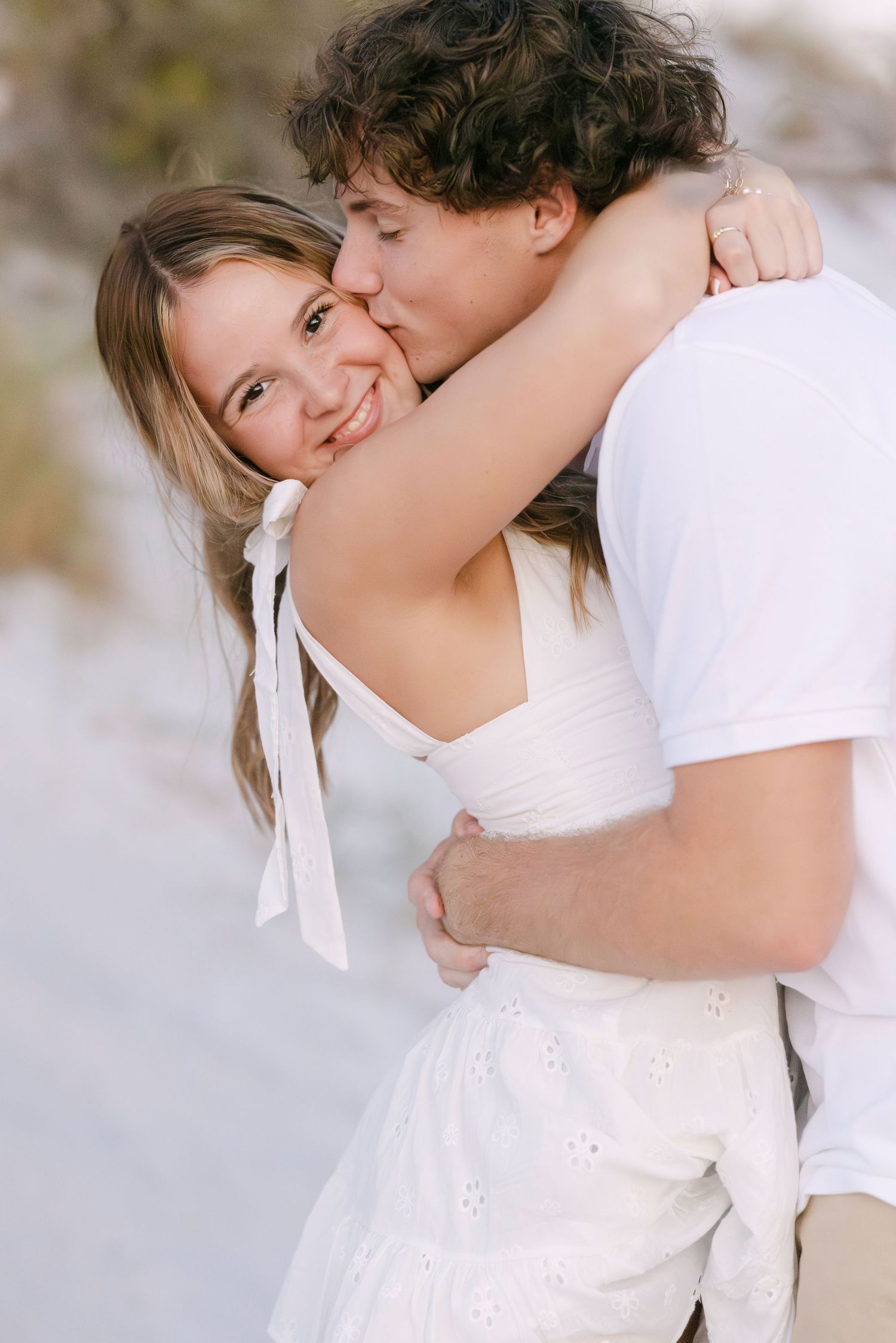Romantic couple in white embracing outdoors with bright smiles and tender affection.