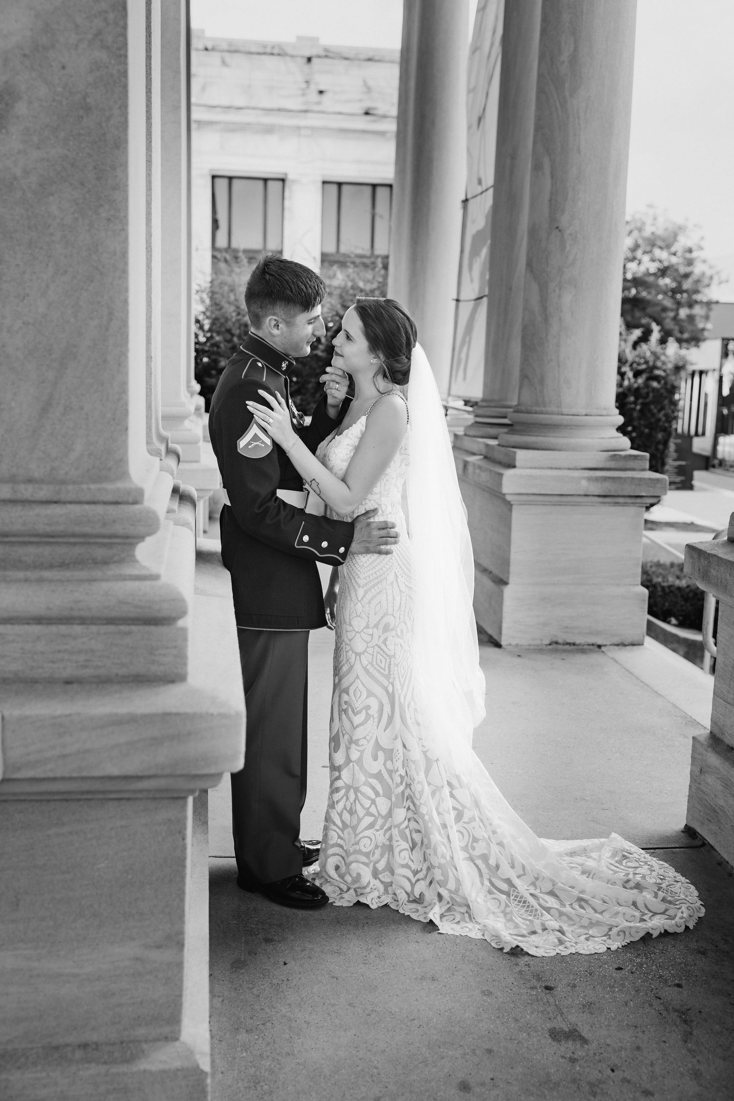 Marine groom and bride share intimate moment between columns in black and white wedding photo.