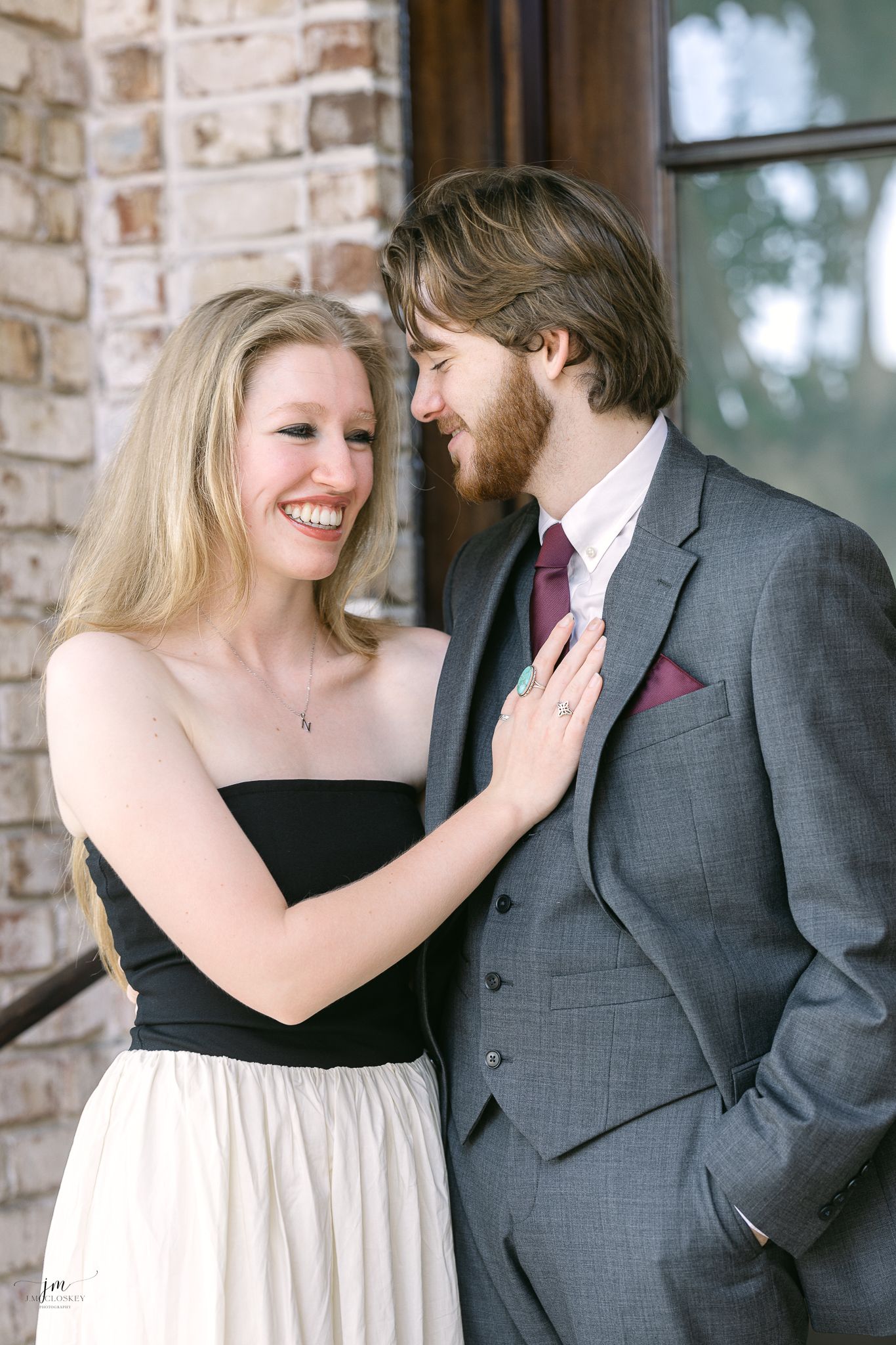 A couple in formal wear embraces on brick steps during a photoshoot.