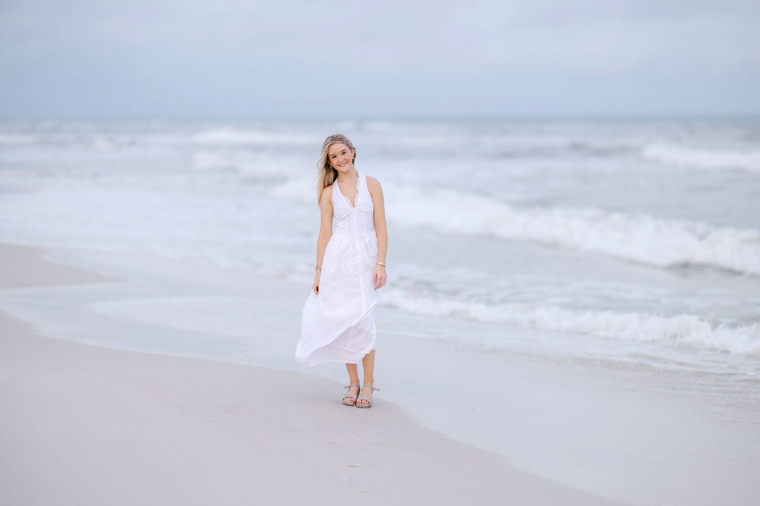 Figure in white dress walking alone on misty beach shoreline.