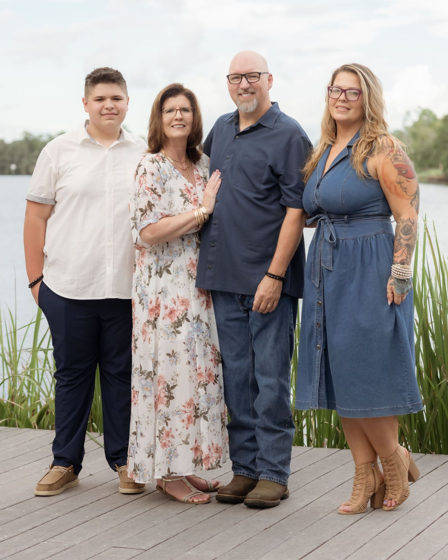 Family of four posing together on a wooden dock near a lake, dressed in smart casual attire for a portrait photo.