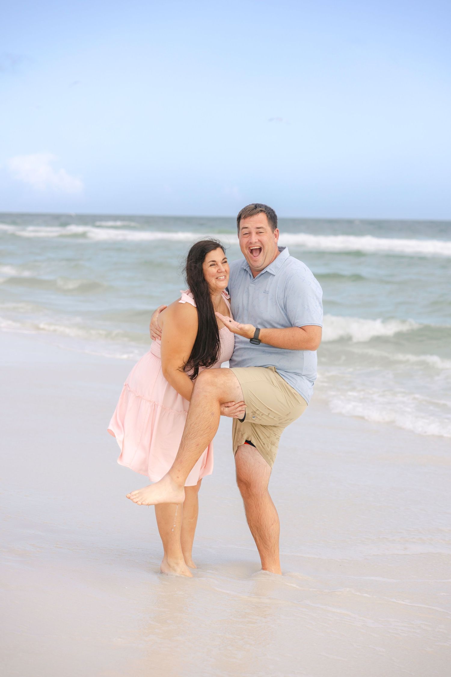 Playful couple enjoying a romantic moment at the beach with waves in the background.