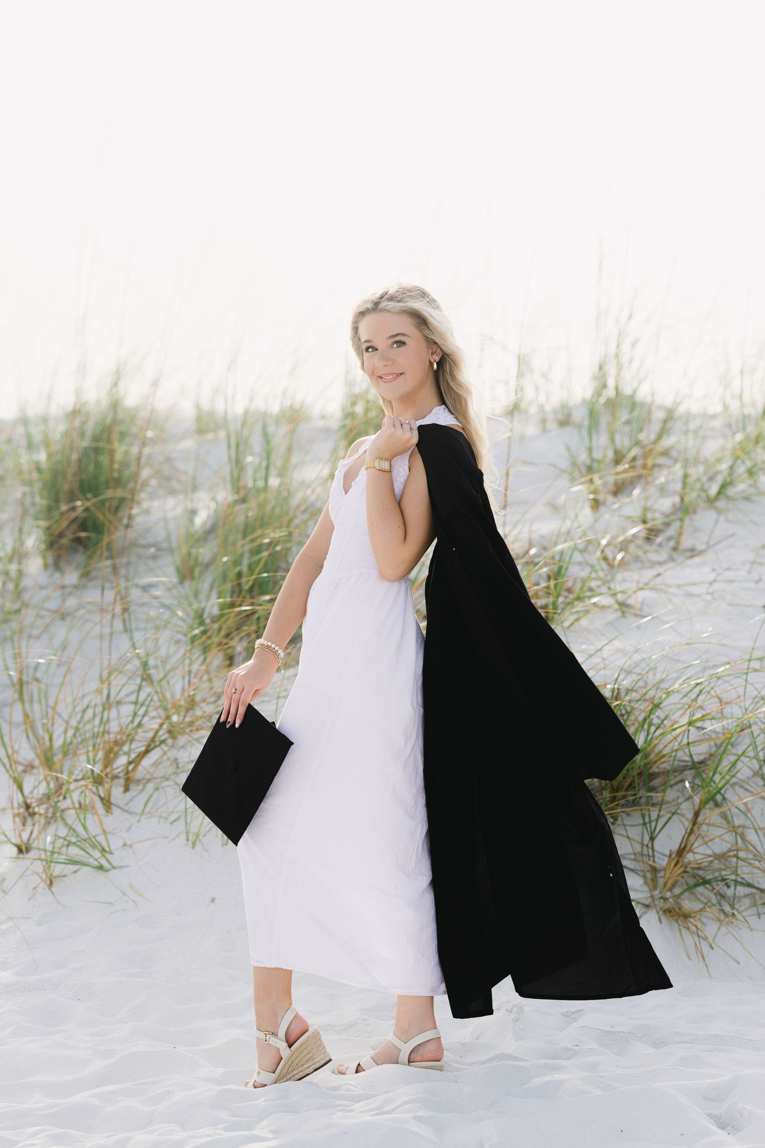 A series of beach portraits showing someone in a white dress and black jacket sitting among sand dunes.