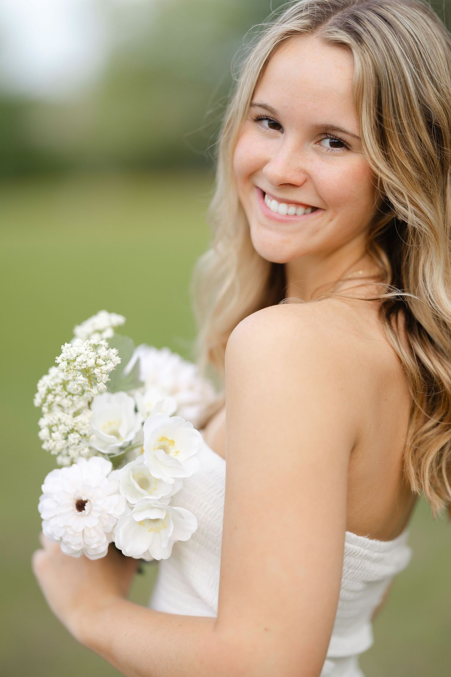 A bride in a white wedding dress poses outdoors while holding a delicate bouquet of baby's breath flowers.