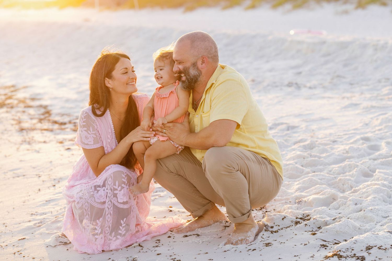 Multiple couples share romantic moments while sitting on a sandy beach during golden hour.