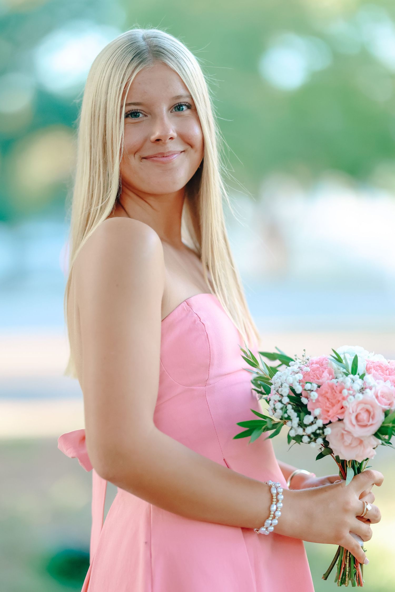 Bridesmaid in a pink strapless dress holds a pink and white floral bouquet while posing outdoors.