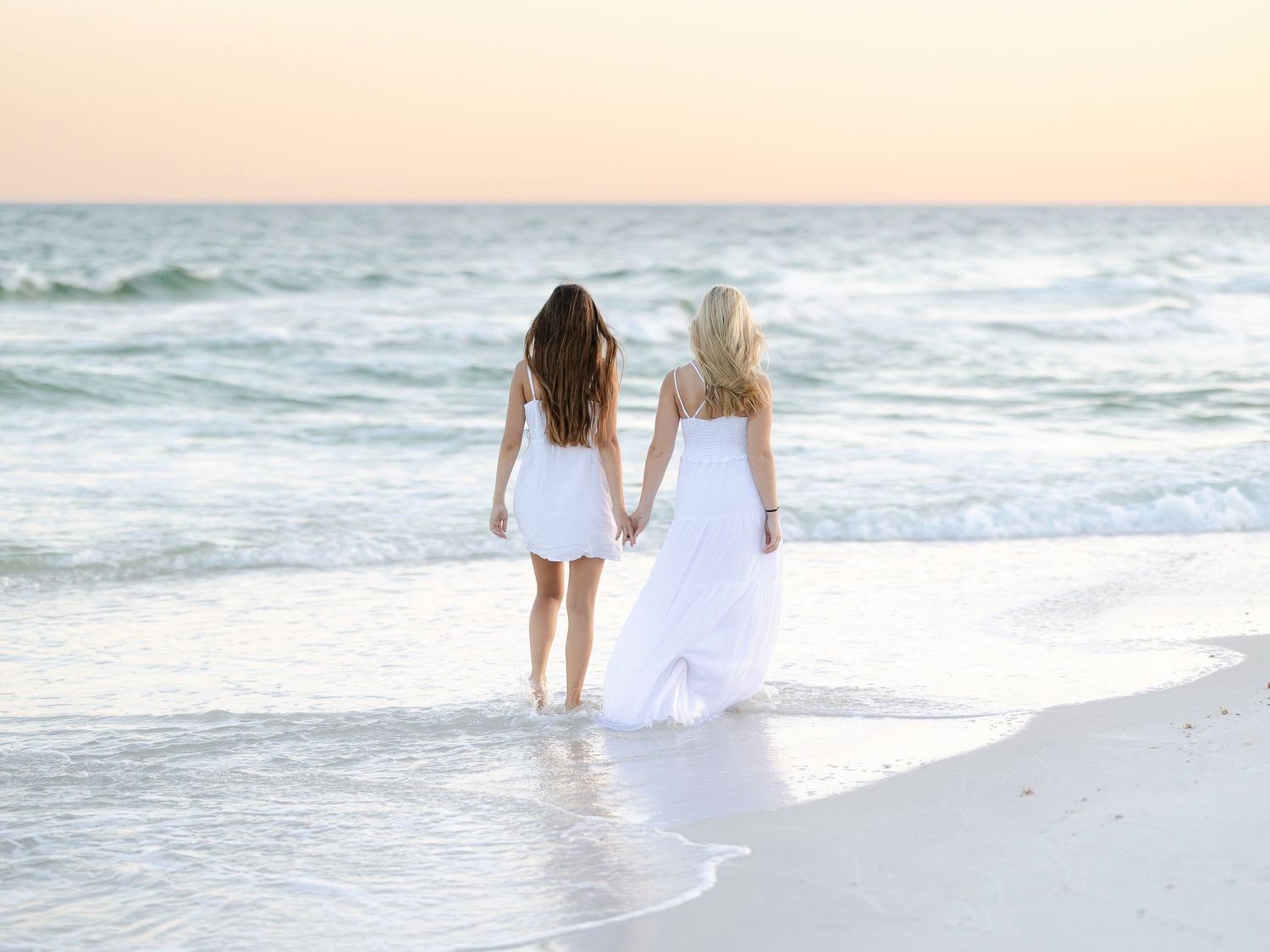Two figures strolling along oceanfront in white clothing at sunset.