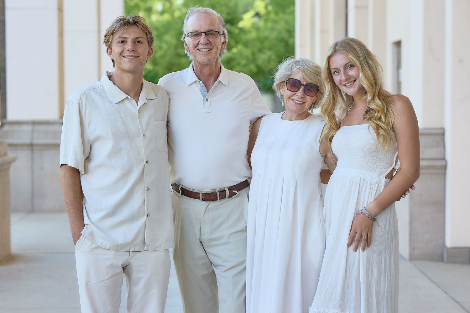 A coordinated family group wearing white outfits poses together outdoors for a photo session.