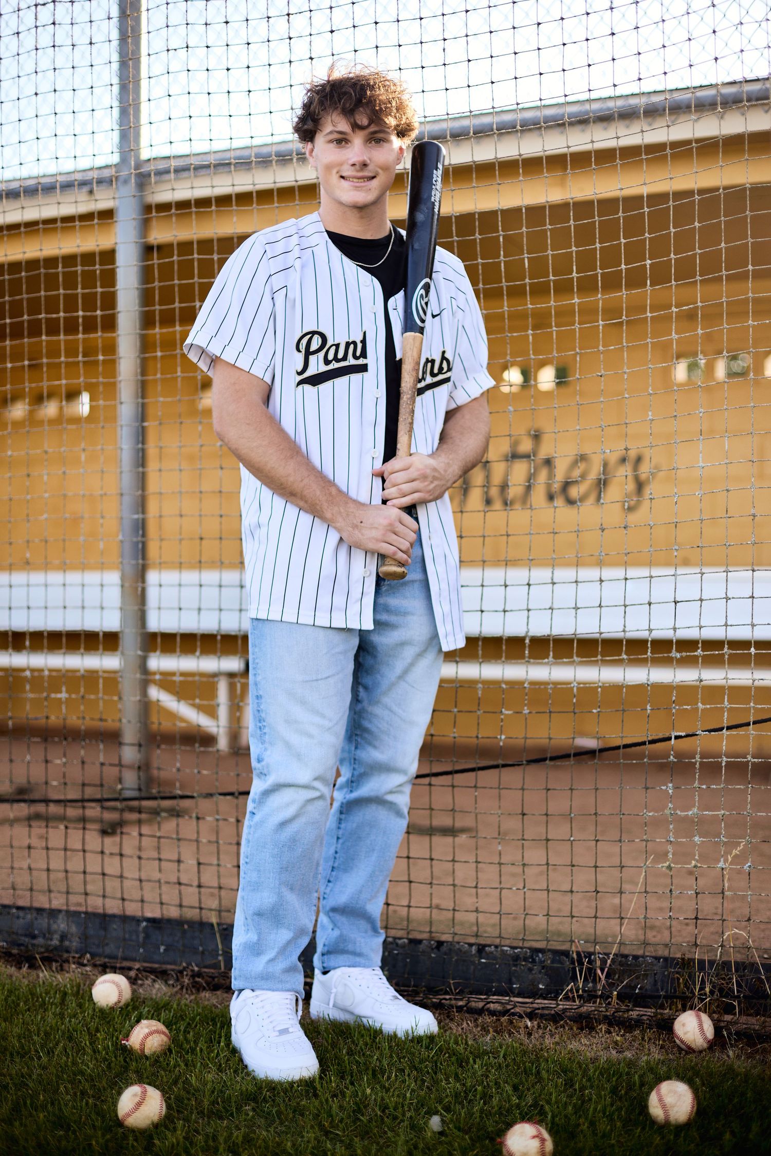 Baseball player in Panthers uniform posing by batting cage with baseballs.