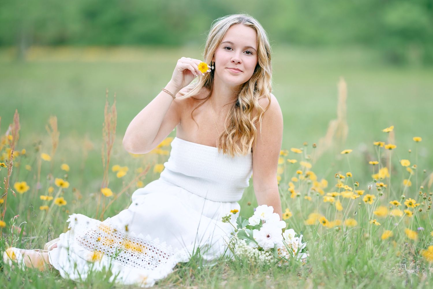 Outdoor summer portrait among yellow wildflowers in white dress.