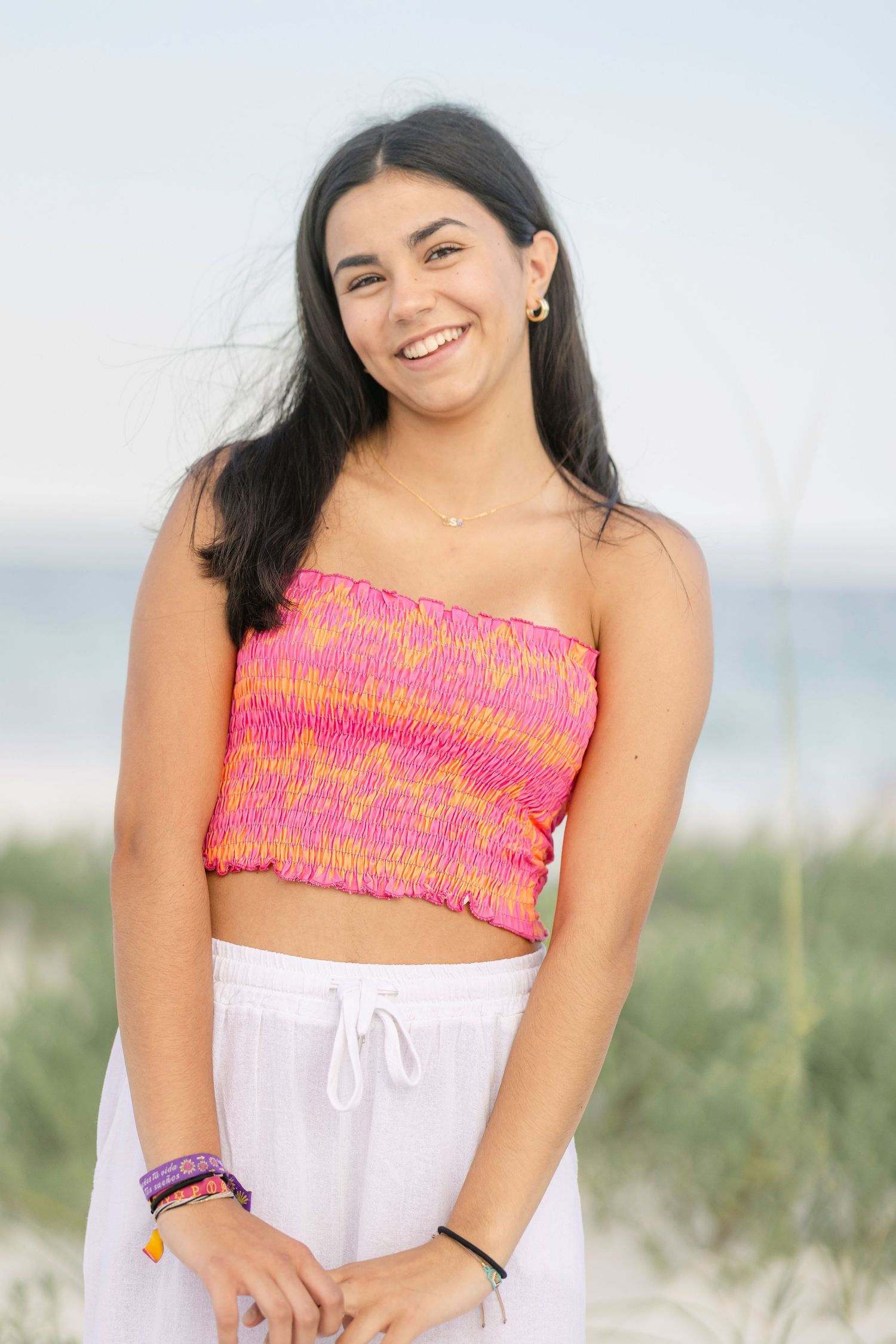 Summer beach style with pink smocked crop top and white pants against coastal backdrop.