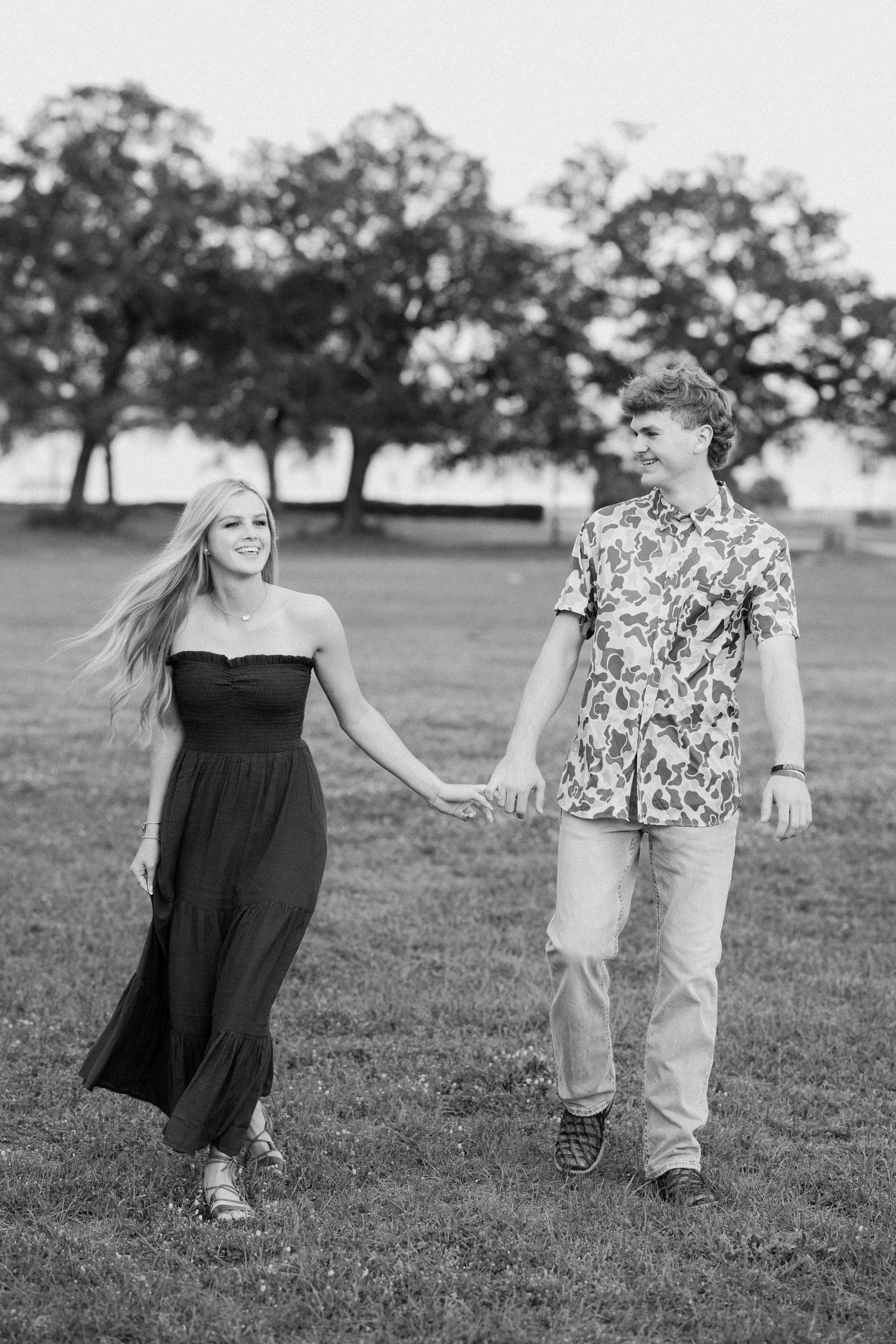 A couple dances playfully in a grassy field during a black and white outdoor photoshoot.