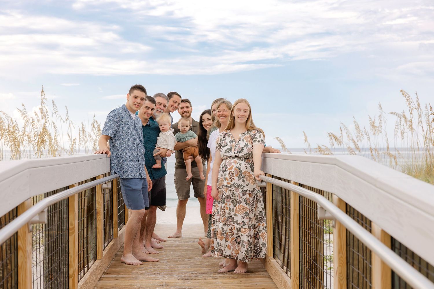 Family gathered on wooden boardwalk overlooking beach with sea oats in foreground.