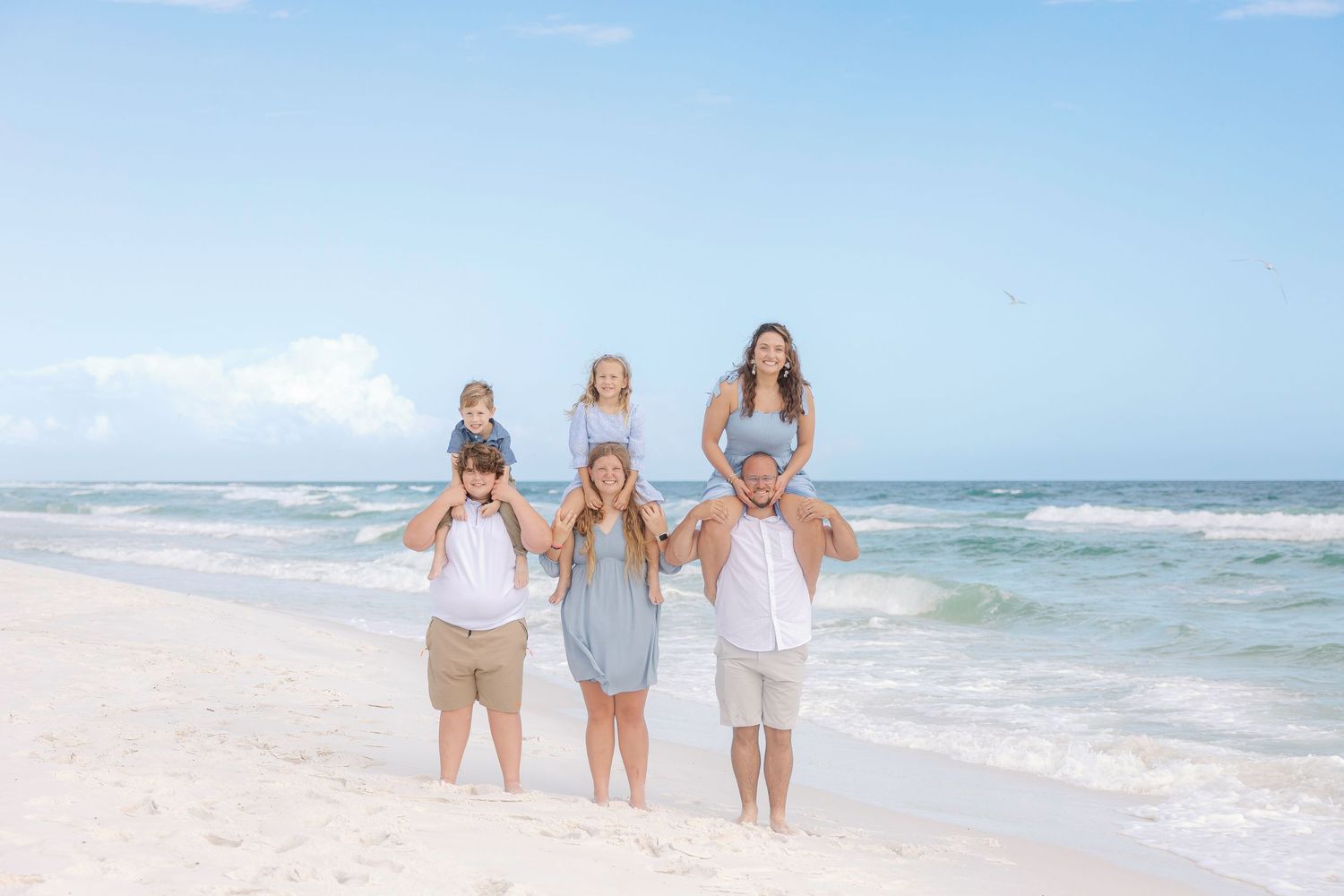 Three people walk along pristine beach shoreline wearing coordinated light colored outfits.