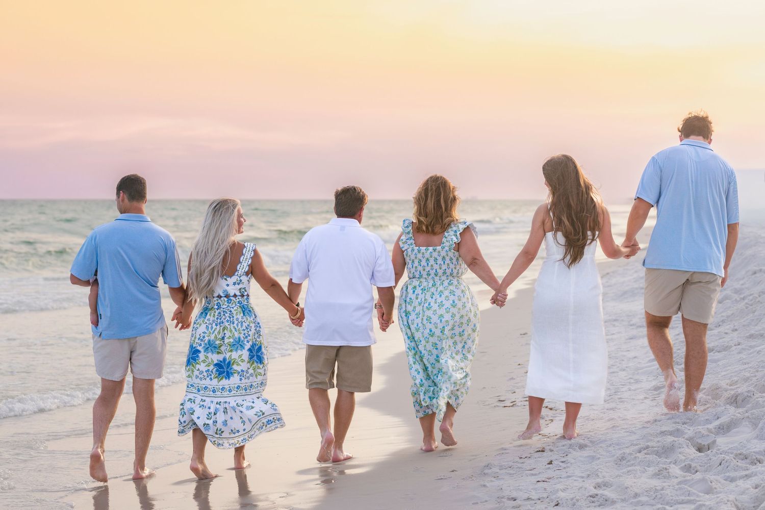 Family of six holding hands walking along a beach at sunset.