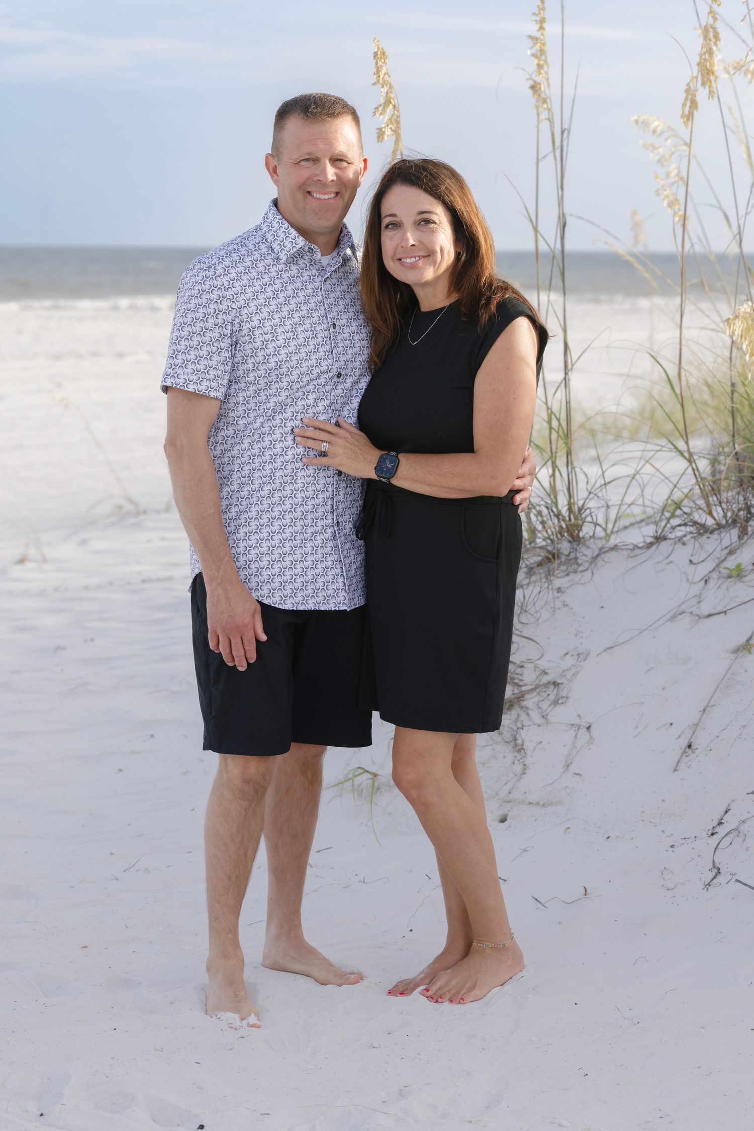 Couple smiling together on a white sand beach near sea oats at sunset.
