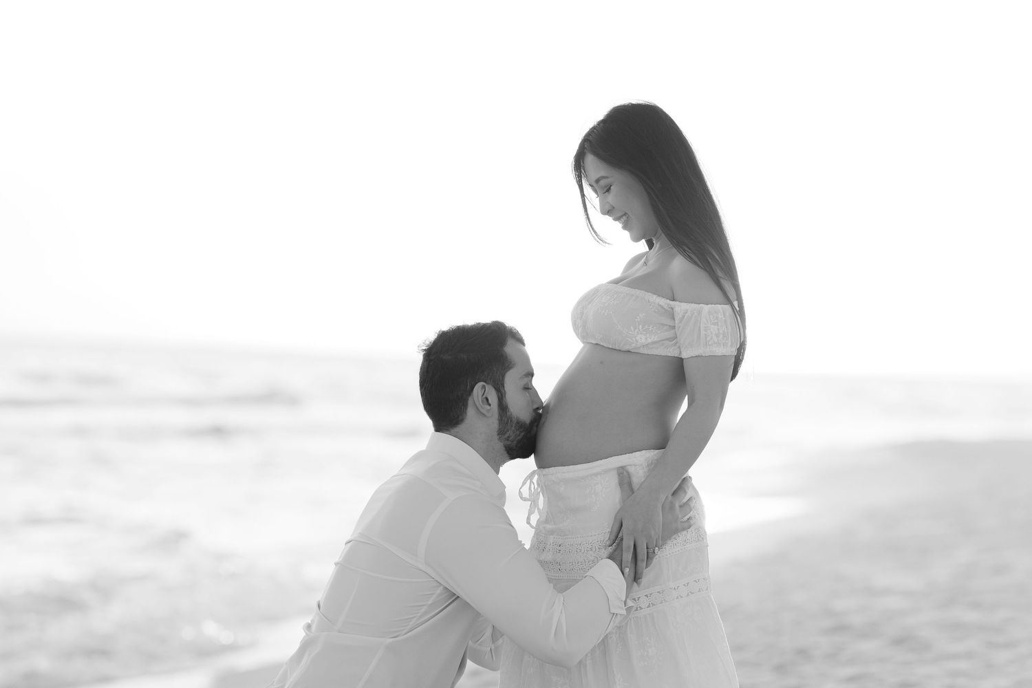 Black and white photo of an expectant couple sharing an intimate moment on the beach.