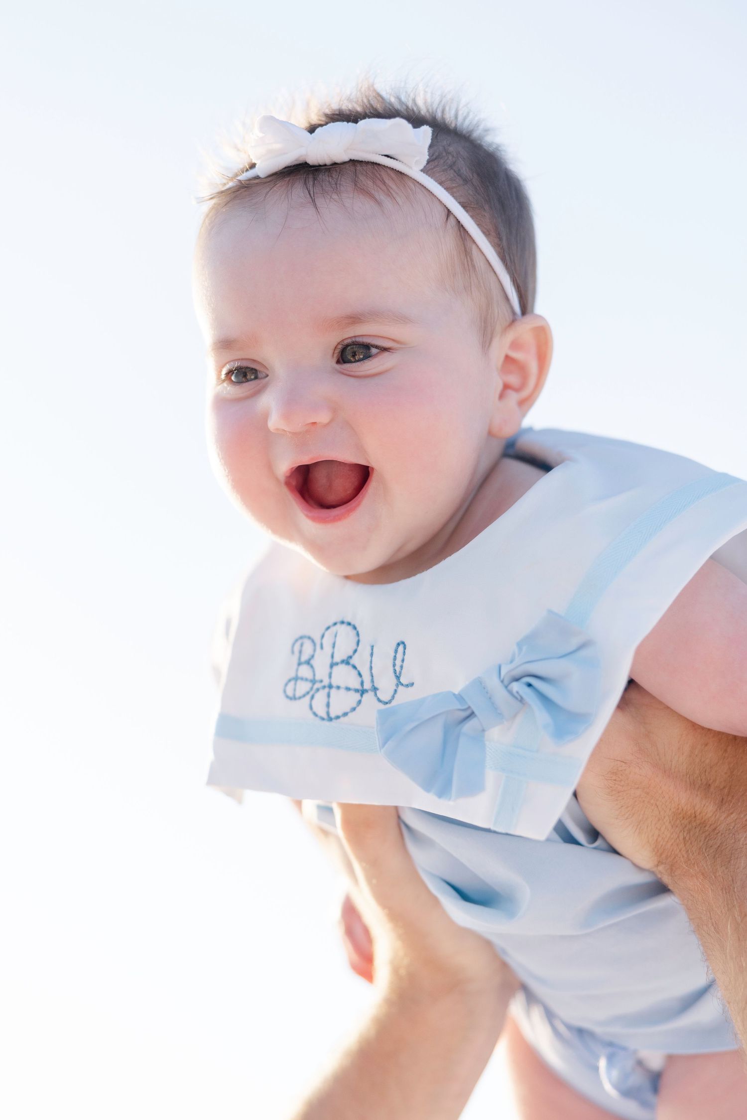Close-up of a happy baby wearing a light blue outfit against bright background.