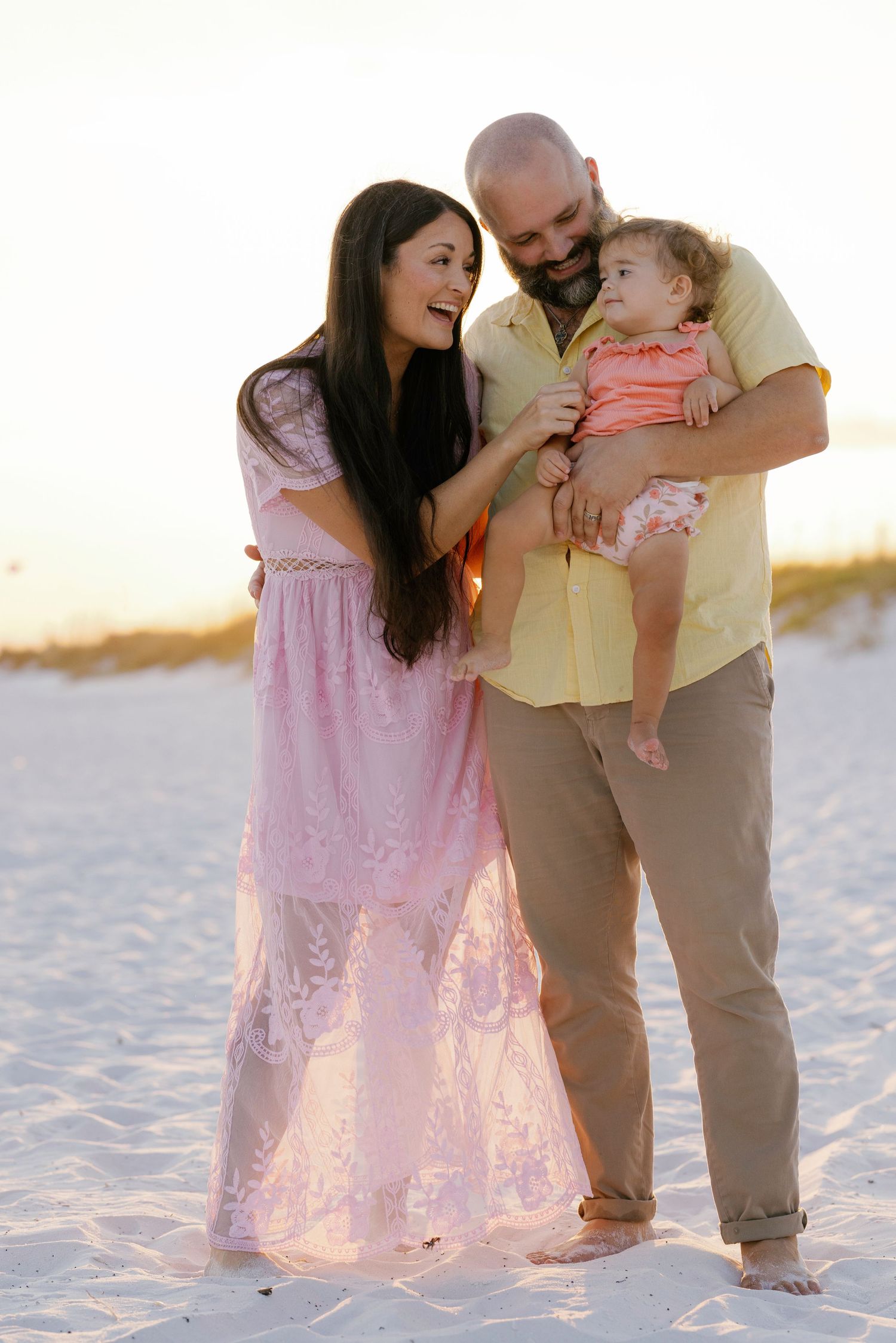 Family in matching pink and yellow outfits shares tender moments together on a sunny beach at sunset.