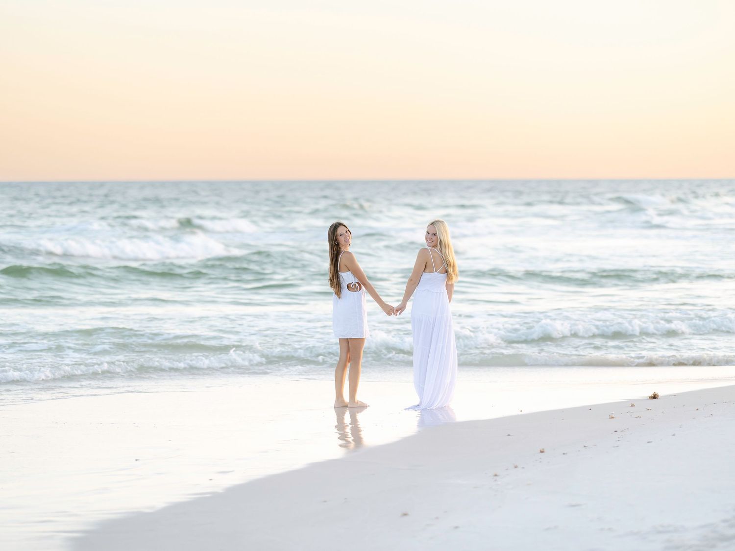 Two people in white outfits walking along shoreline during golden hour.