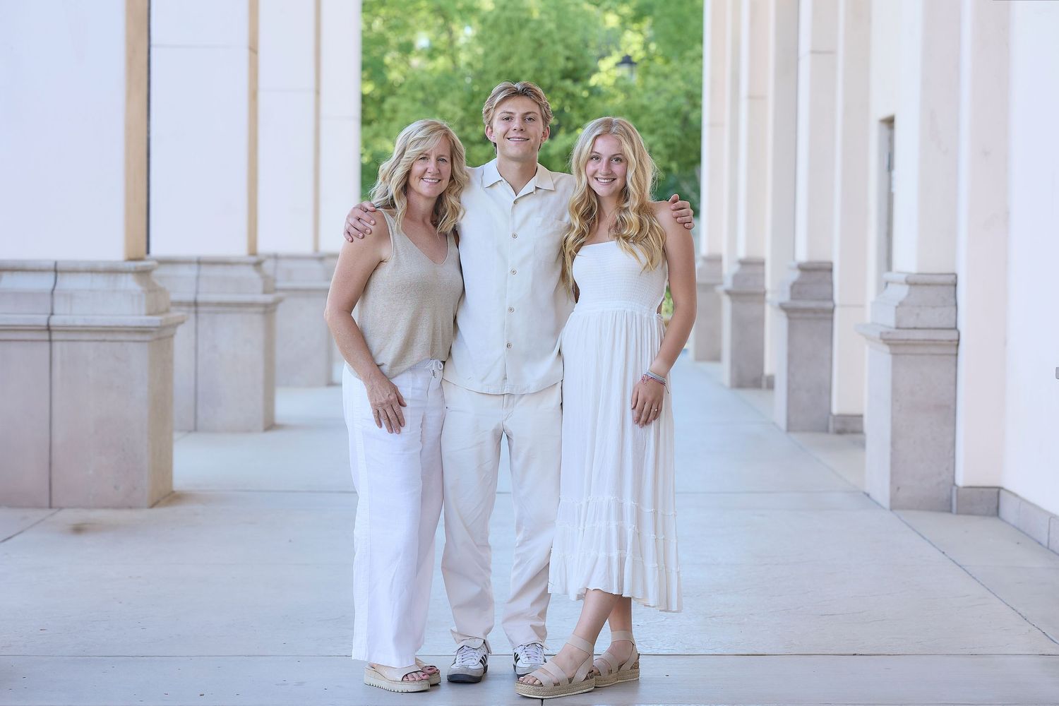 Four people in coordinated white outfits pose together for elegant family portraits against a columned building exterior.